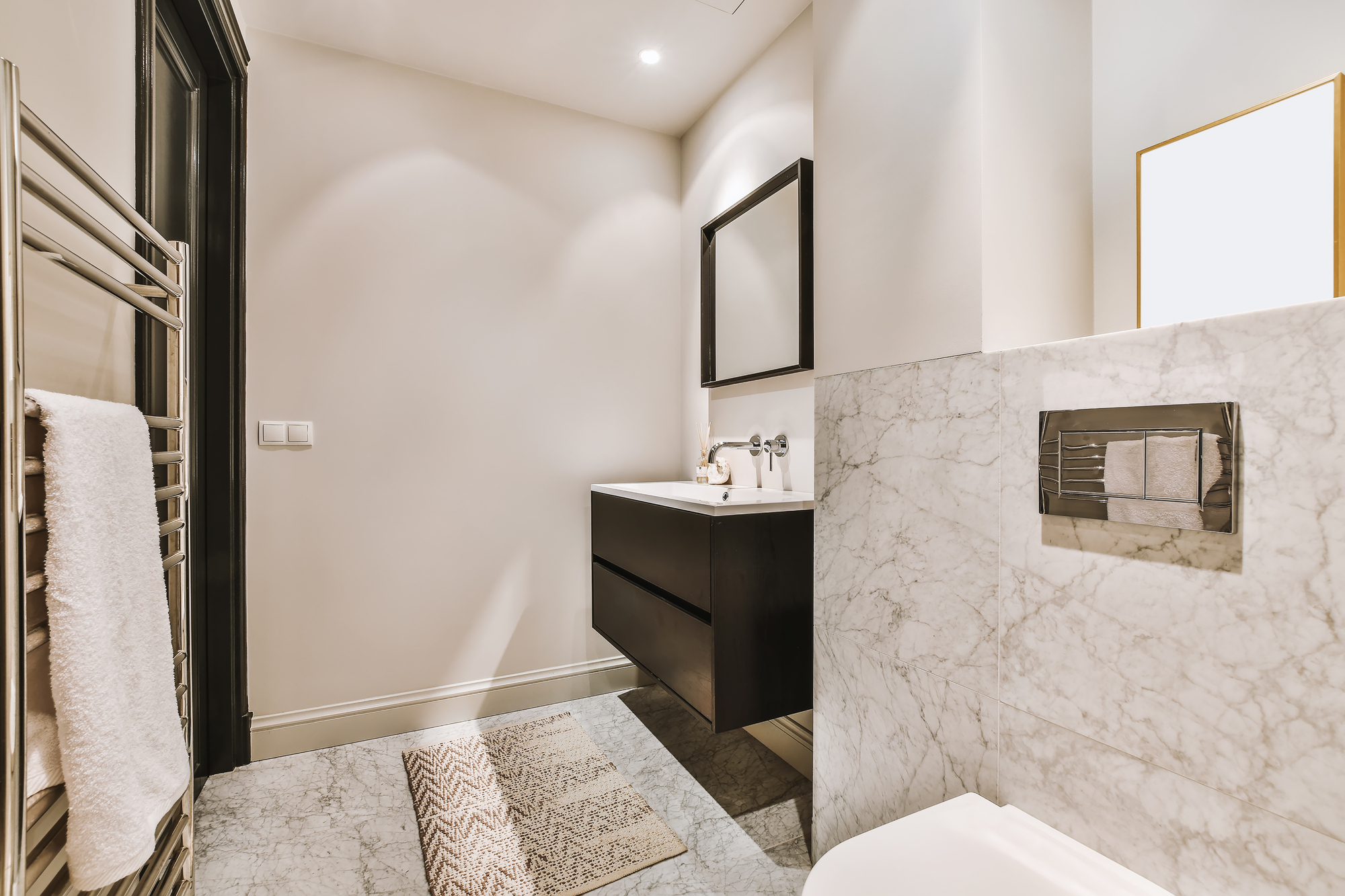 A luxury remodeled bathroom with marble walls and a vanity with a mirror above it.