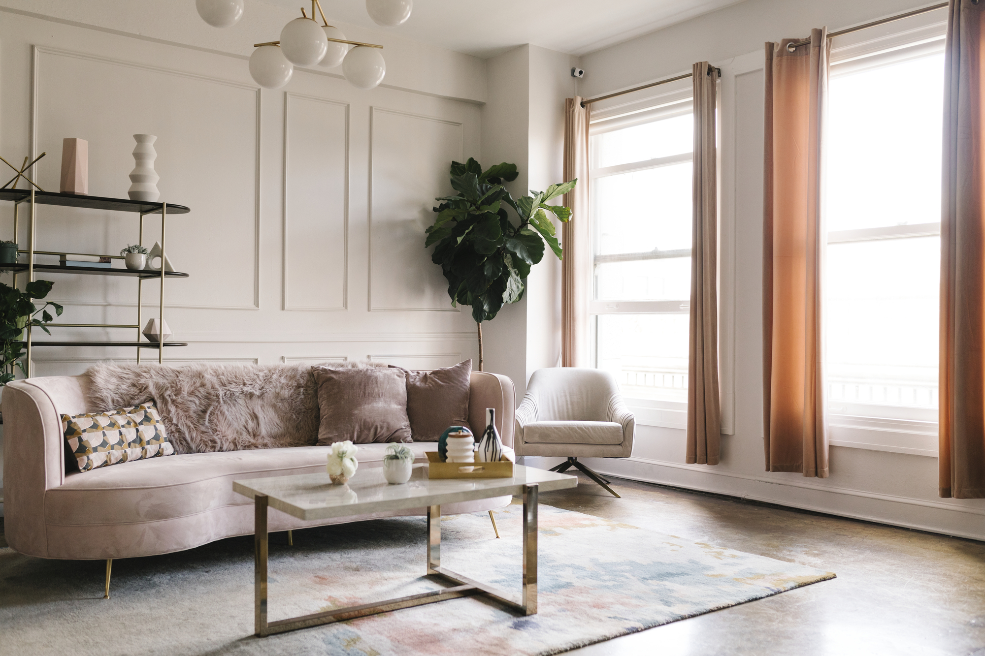 A living room with a couch, chair, and marble table with ball lights above and curtains on the tall windows.