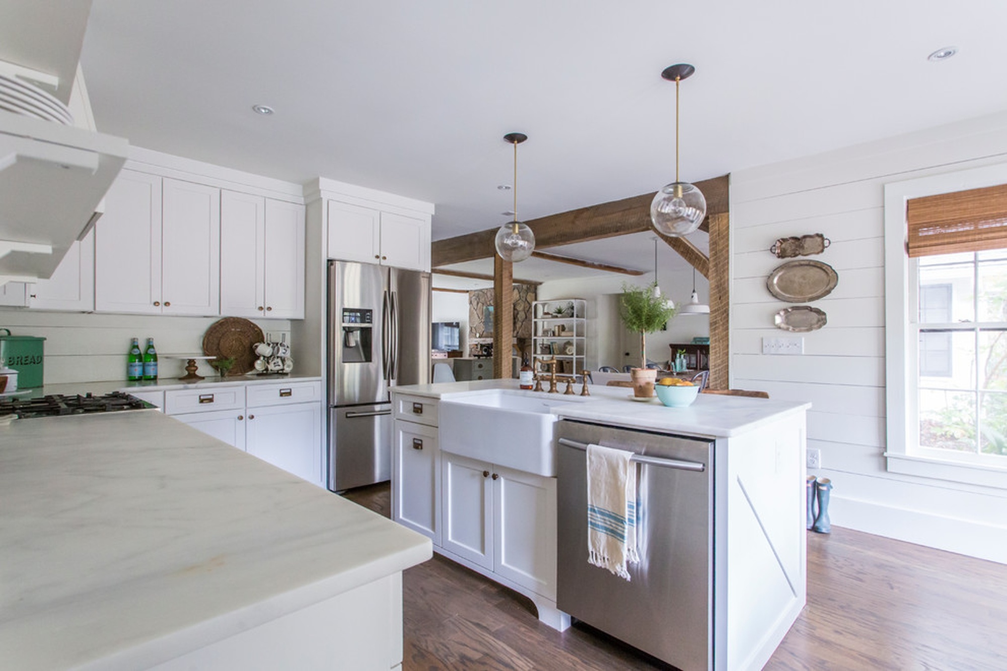 A kitchen with marble countertops, a white island, lights hanging from the ceiling, and a silver refrigerator in the background.