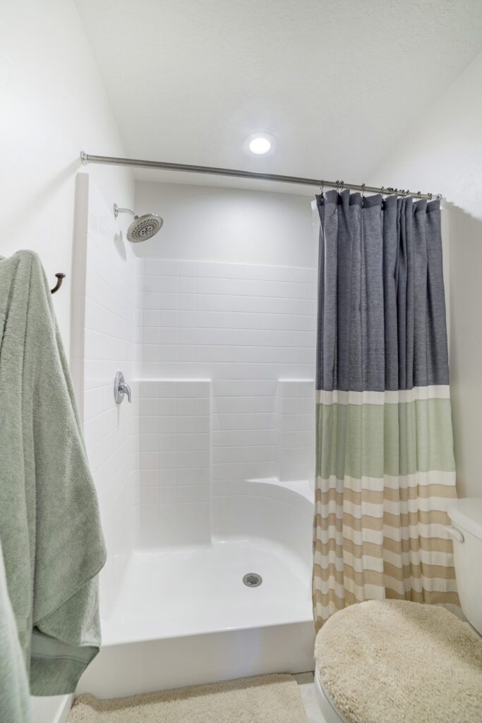 An acrylic shower with a pastel shower curtain, silver showerhead, and a towel on the wall.