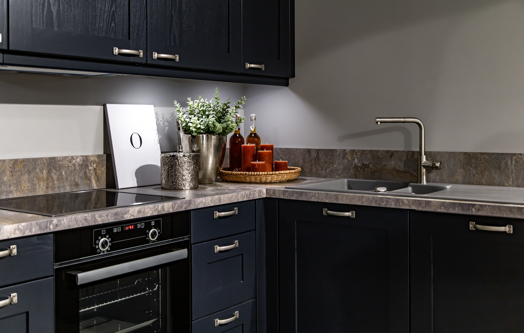 The corner of a kitchen with blue drawers, cabinets, and a tile countertop with a sink.