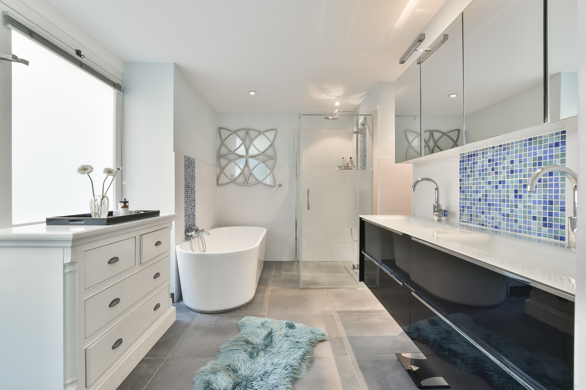 A modern bathroom with a white vanity, white drawers, a white freestanding bathtub, and a walk-in shower with a glass door.