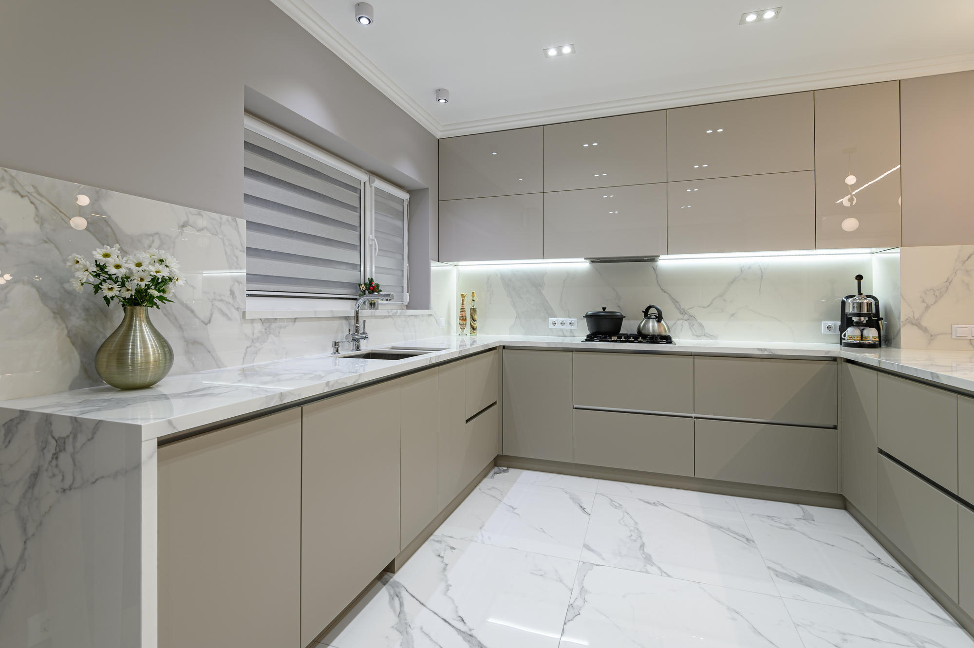A modern kitchen with marble countertops and tan drawers.