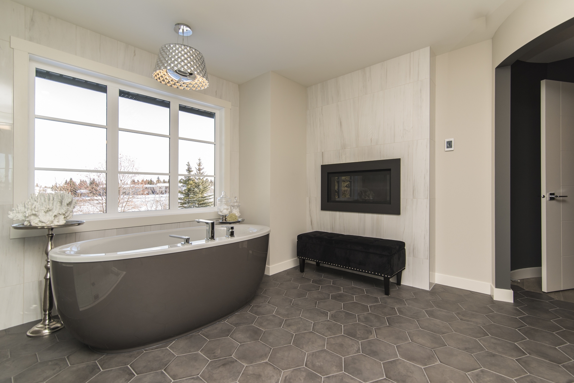 A bathroom with a gray honeycomb floor with a gray freestanding bathtub and windows look outside.