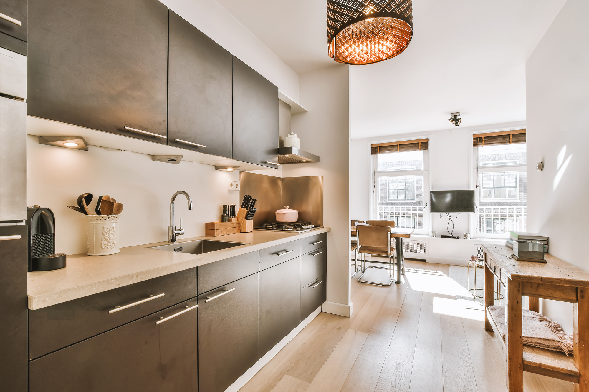 A modern kitchen with hardwood floors, white walls, brown cupboards, and a marble countertop.