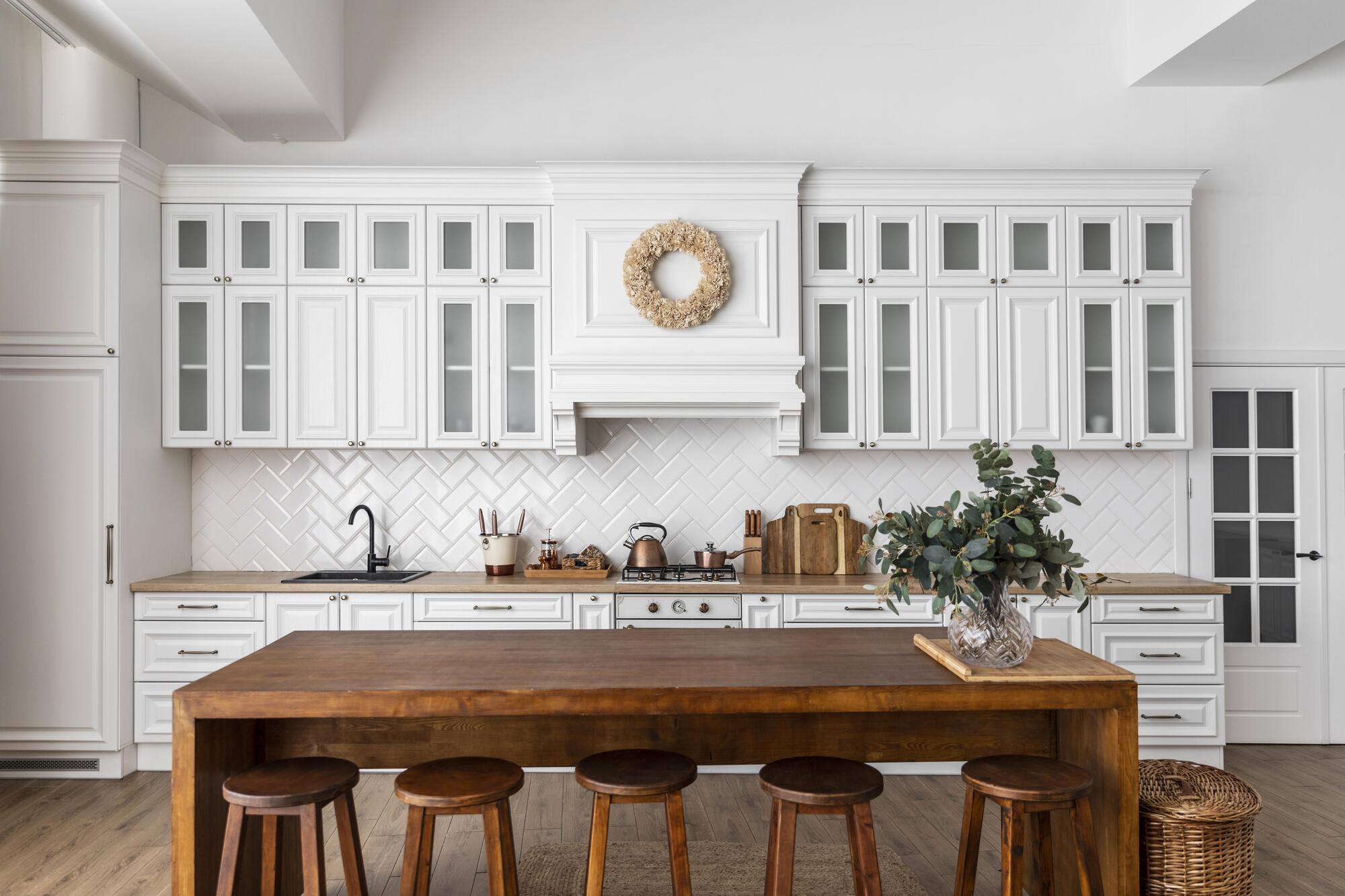 A kitchen with white walls, white cabinets with small windows, wood countertops, and a wood table with stools underneath.