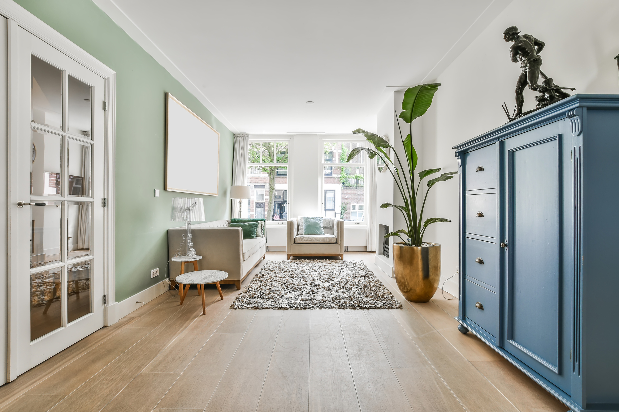 A living room with hardwood flooring, white walls, a blue cabinet, and tan furniture