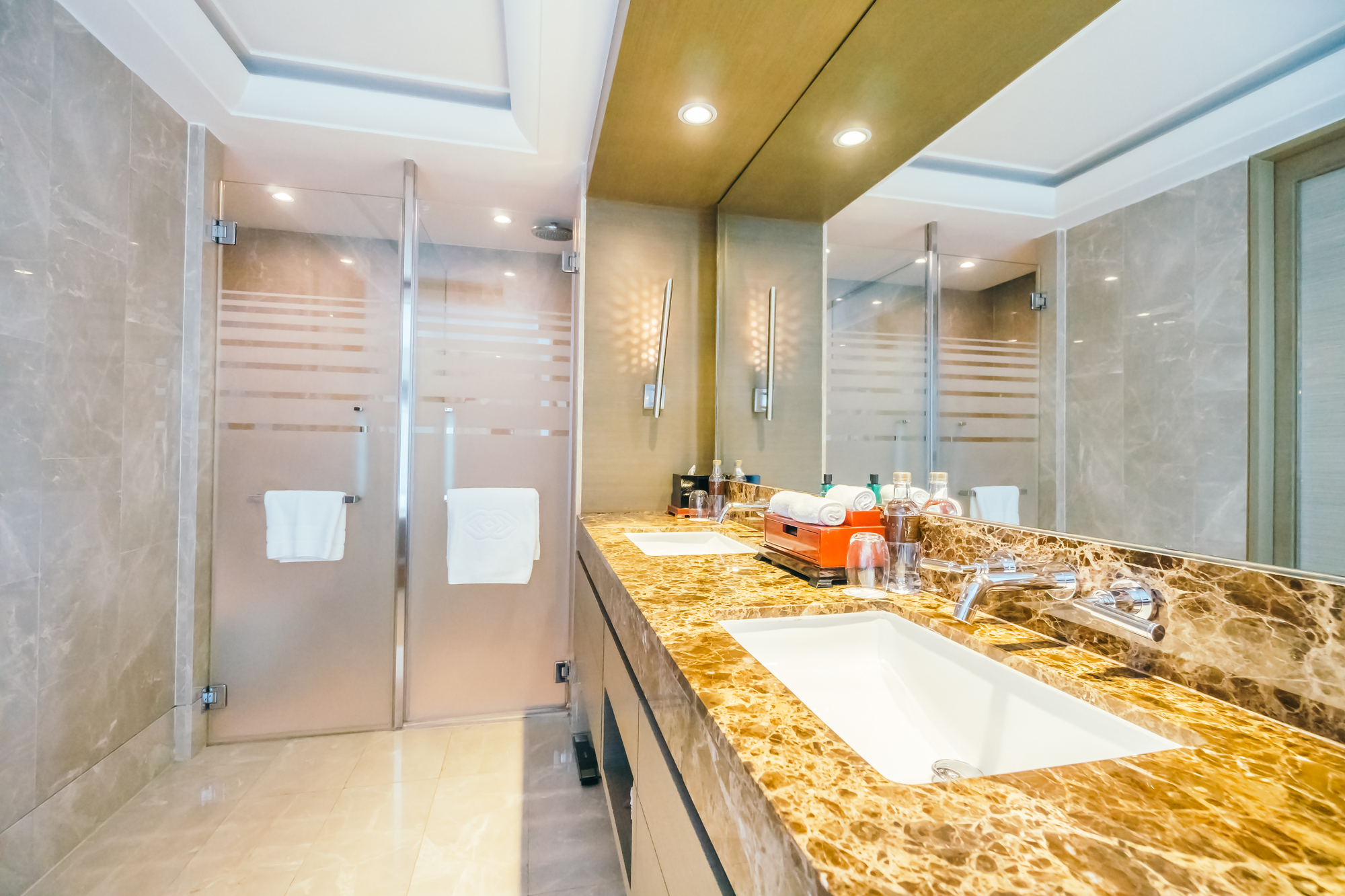 A bathroom with a marble countertop, two sinks, and a walk-in shower with a glass door.
