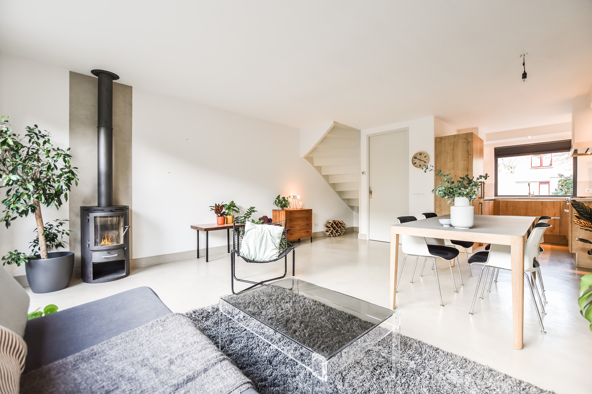 A modern living room with white walls, furniture, and a wooden kitchen table with chairs.
