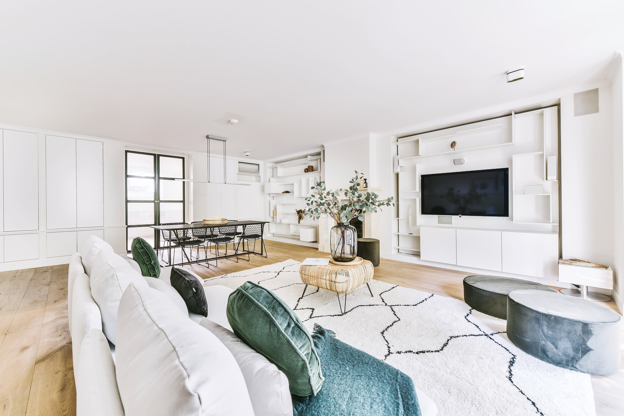 A spacious living room with a white coach, a black table, and a television on the white wall.