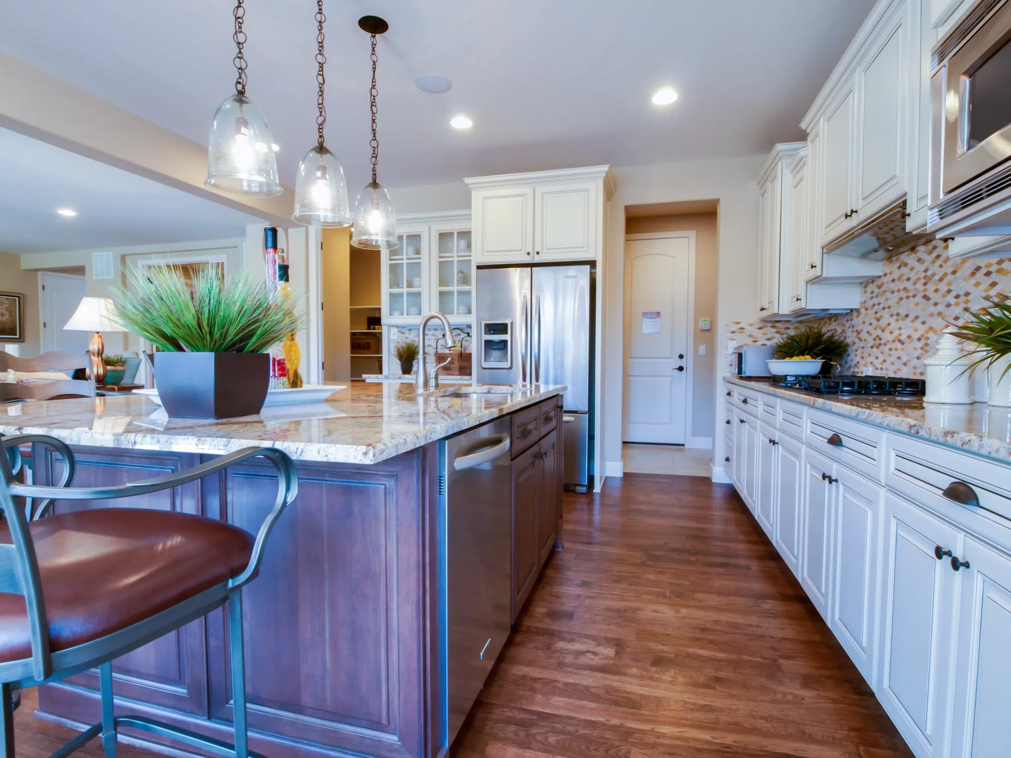 A kitchen with hardwood floors, a kitchen island, and white cabinets with a steel refrigerator in the background.