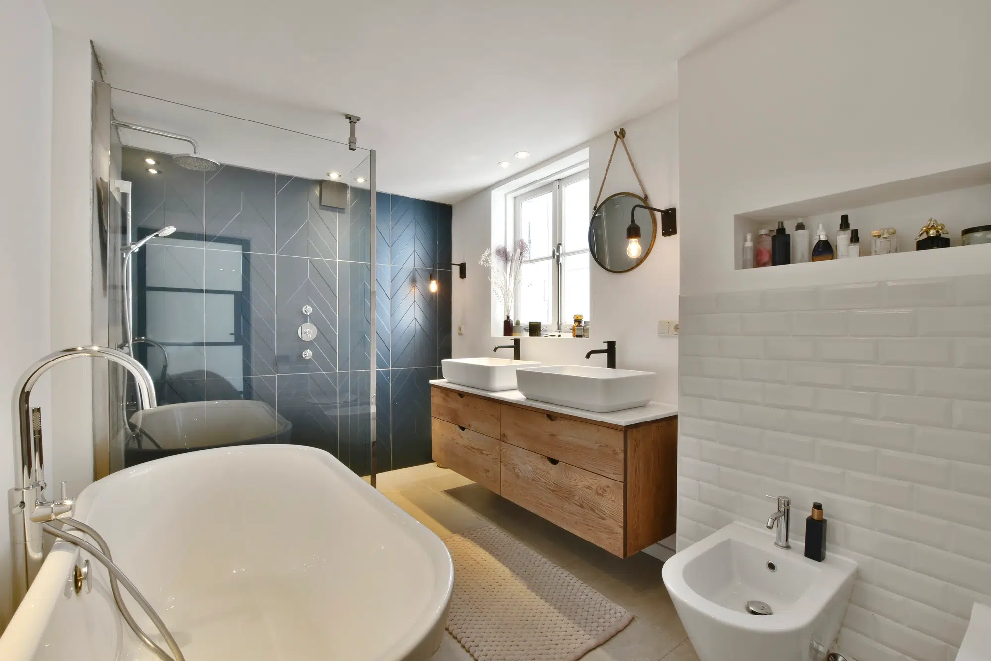 A bathroom with white and blue walls, a white bathtub, and wooden vanity, and a walk-in shower with a glass door.