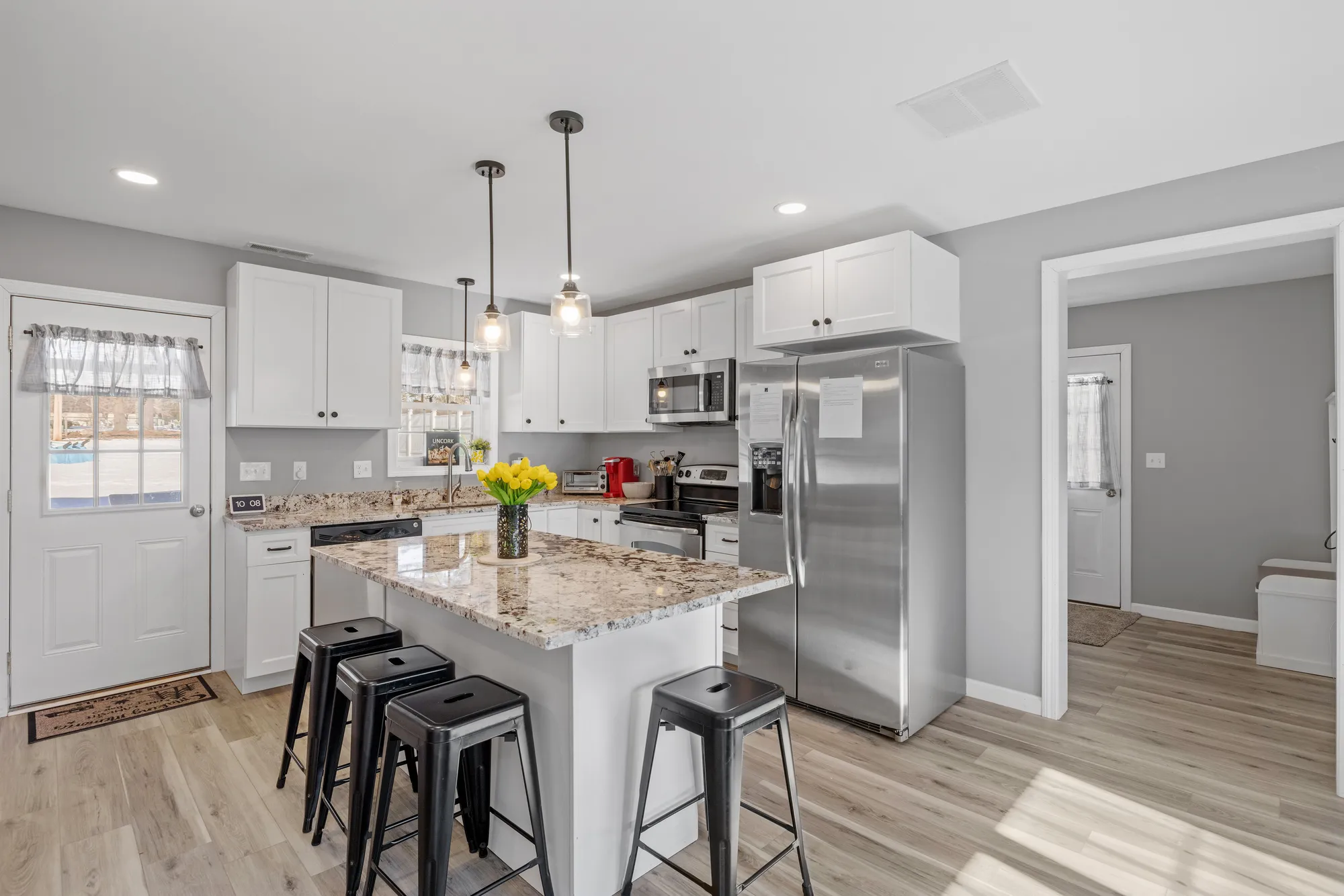 A kitchen with a marble island, black stools, white cabinets, and a steel refrigerator.