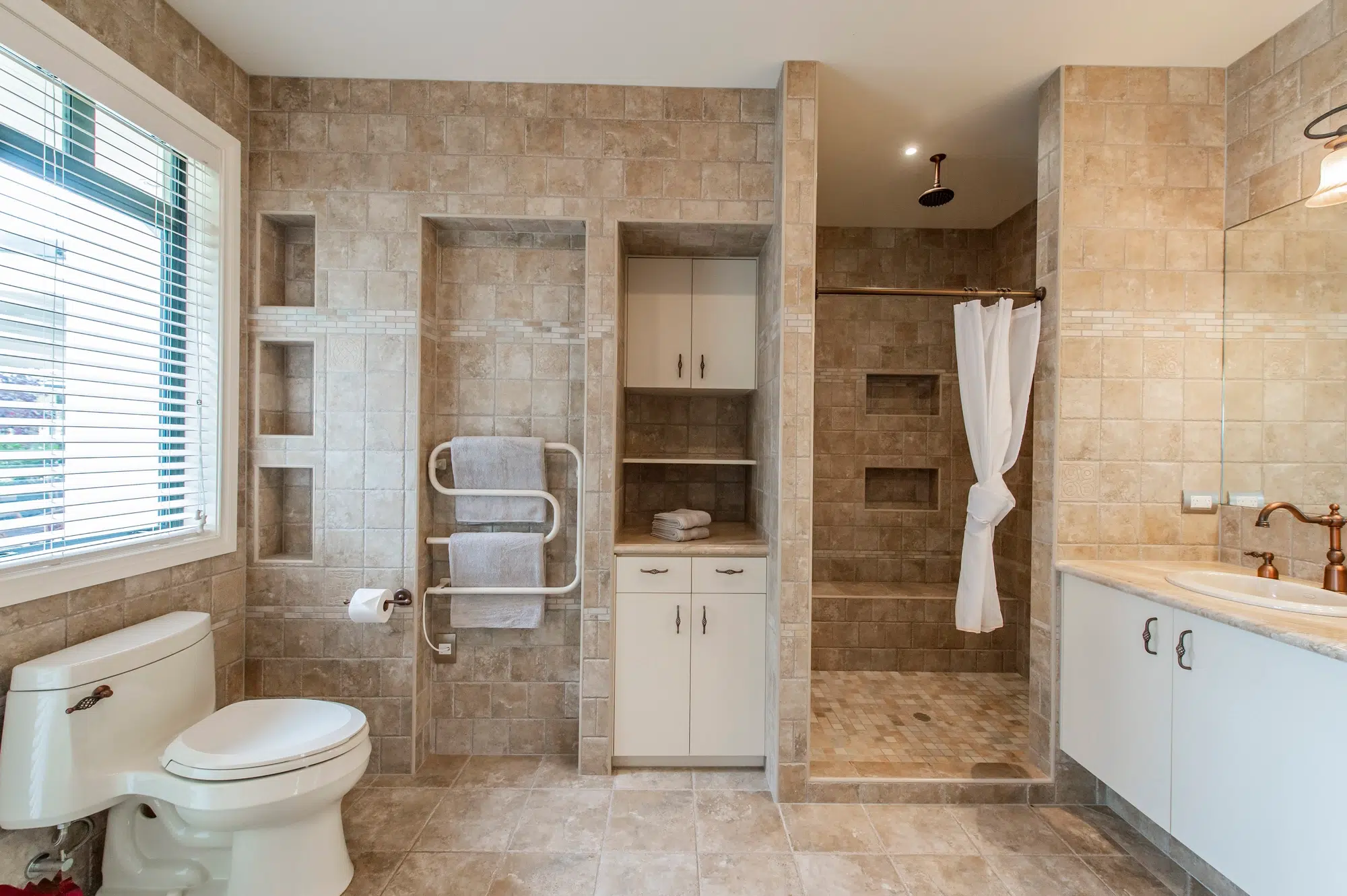 A bathroom with tan walls, a white toilet, white cabinets, and a walk-in shower with a white curtain.