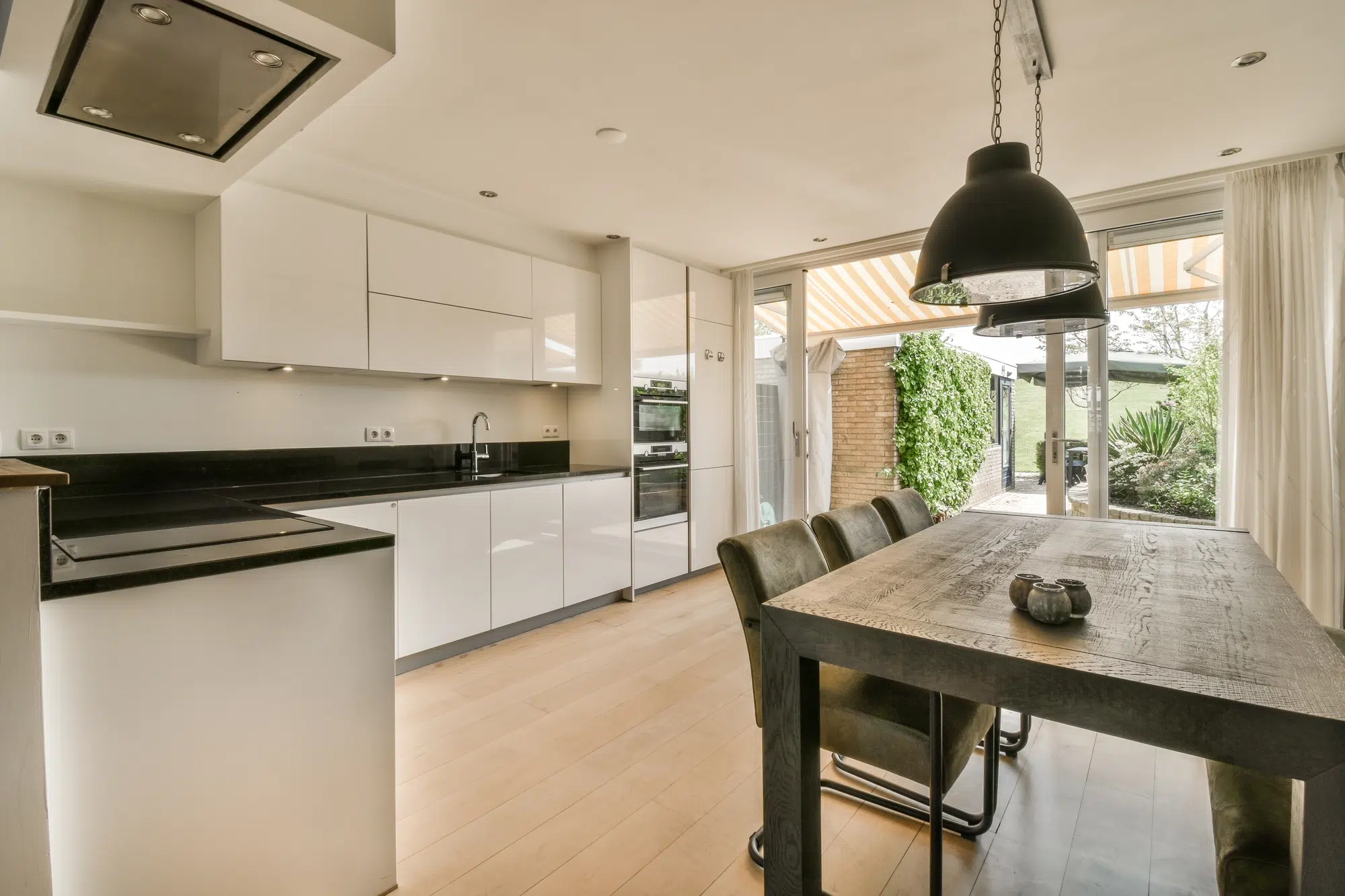 A kitchen with a large wooden table, white cabinets, and black countertops with a sliding glass door leading outside.