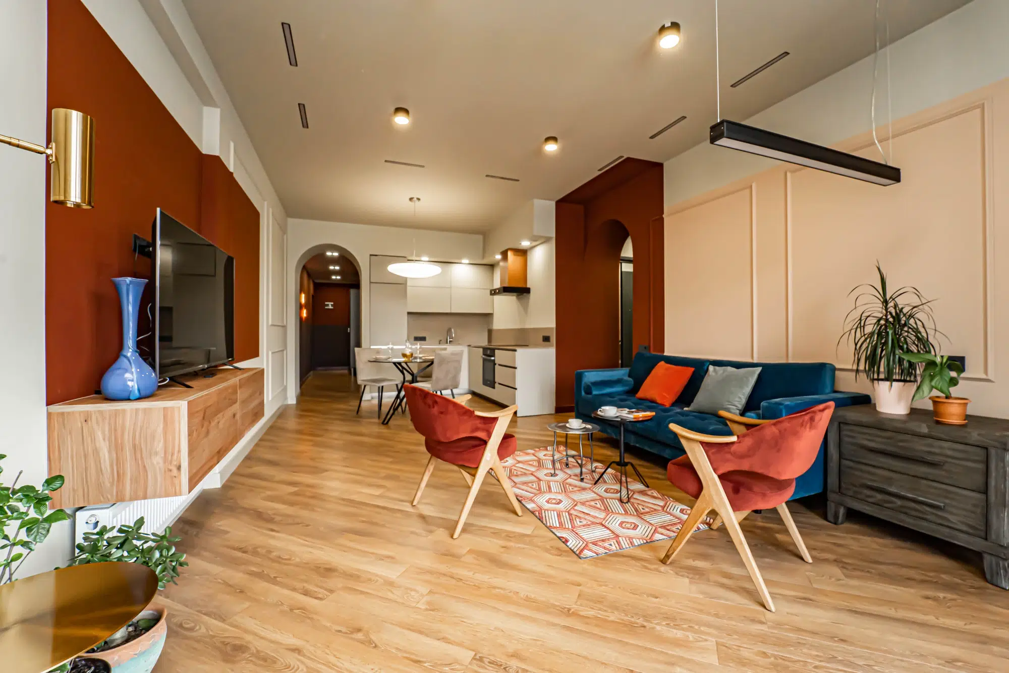 A living room with red and yellow walls, hardwood floors, two wooden chairs, a blue couch, and a television.