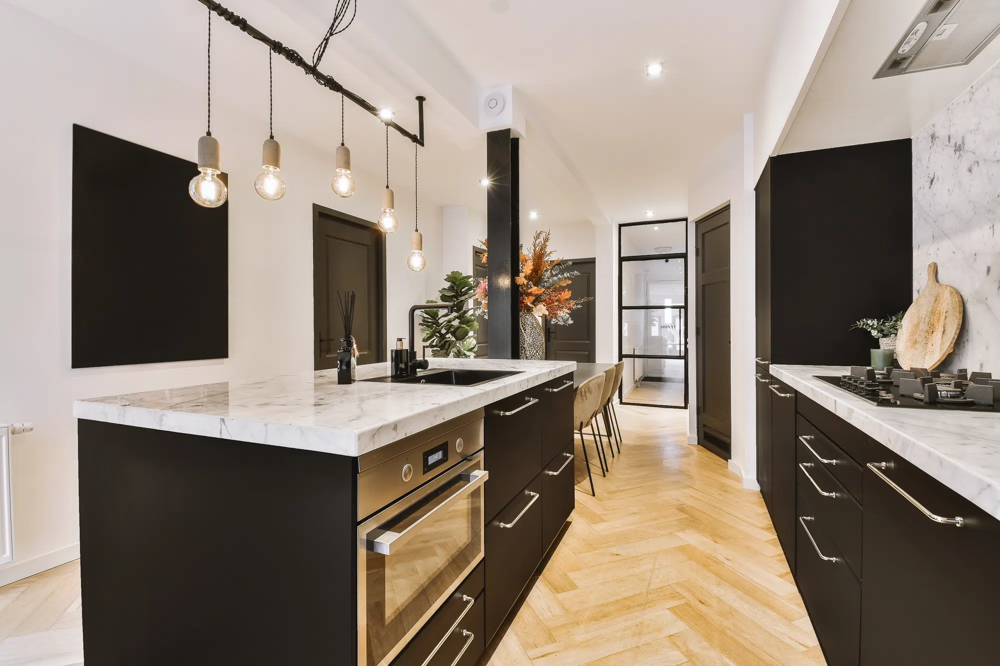 A kitchen with white walls, marble countertops, black cabinets, and a steel oven.
