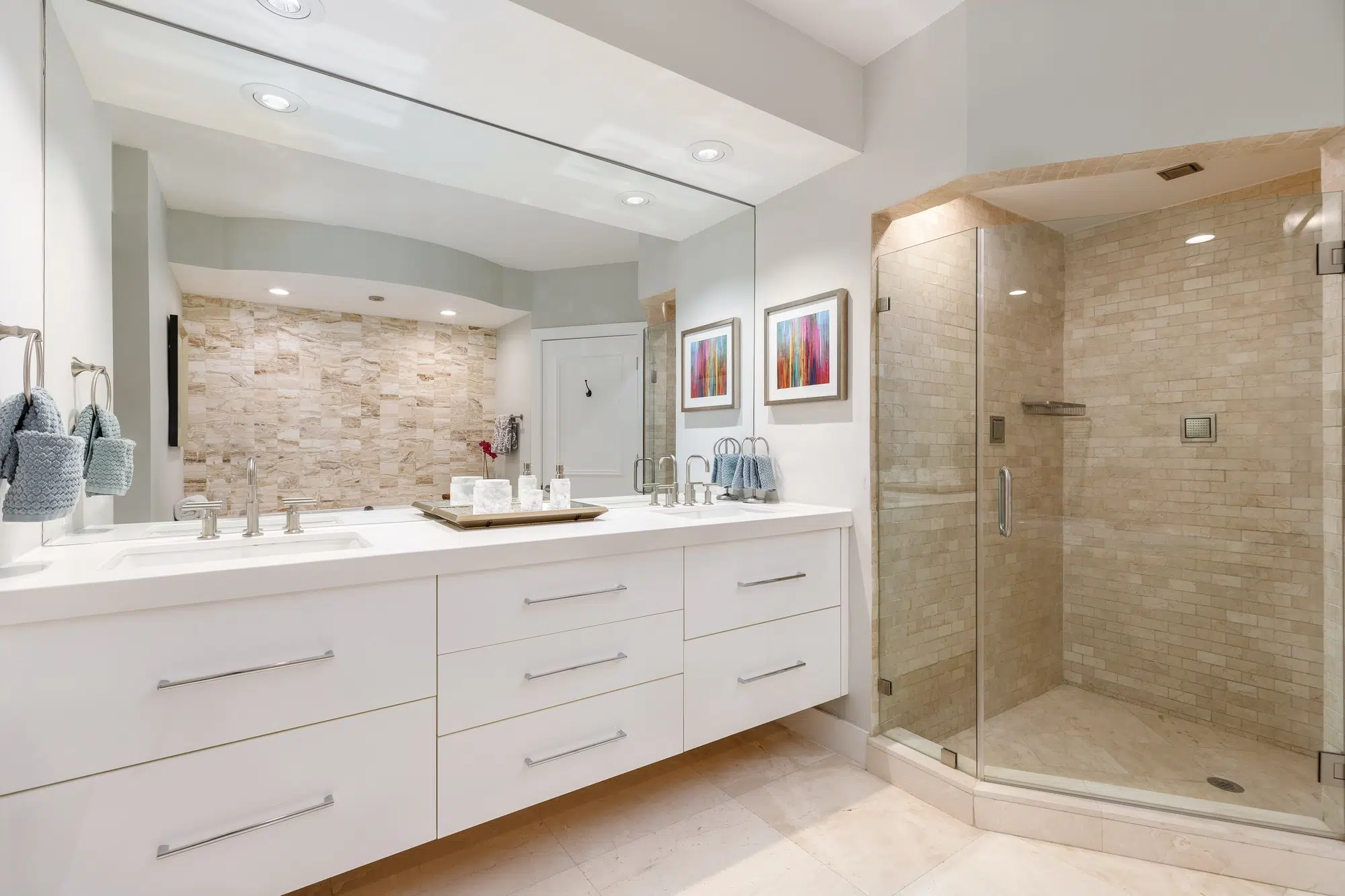 A white bathroom with a white vanity, a large mirror, and a walk-in shower with a glass door.