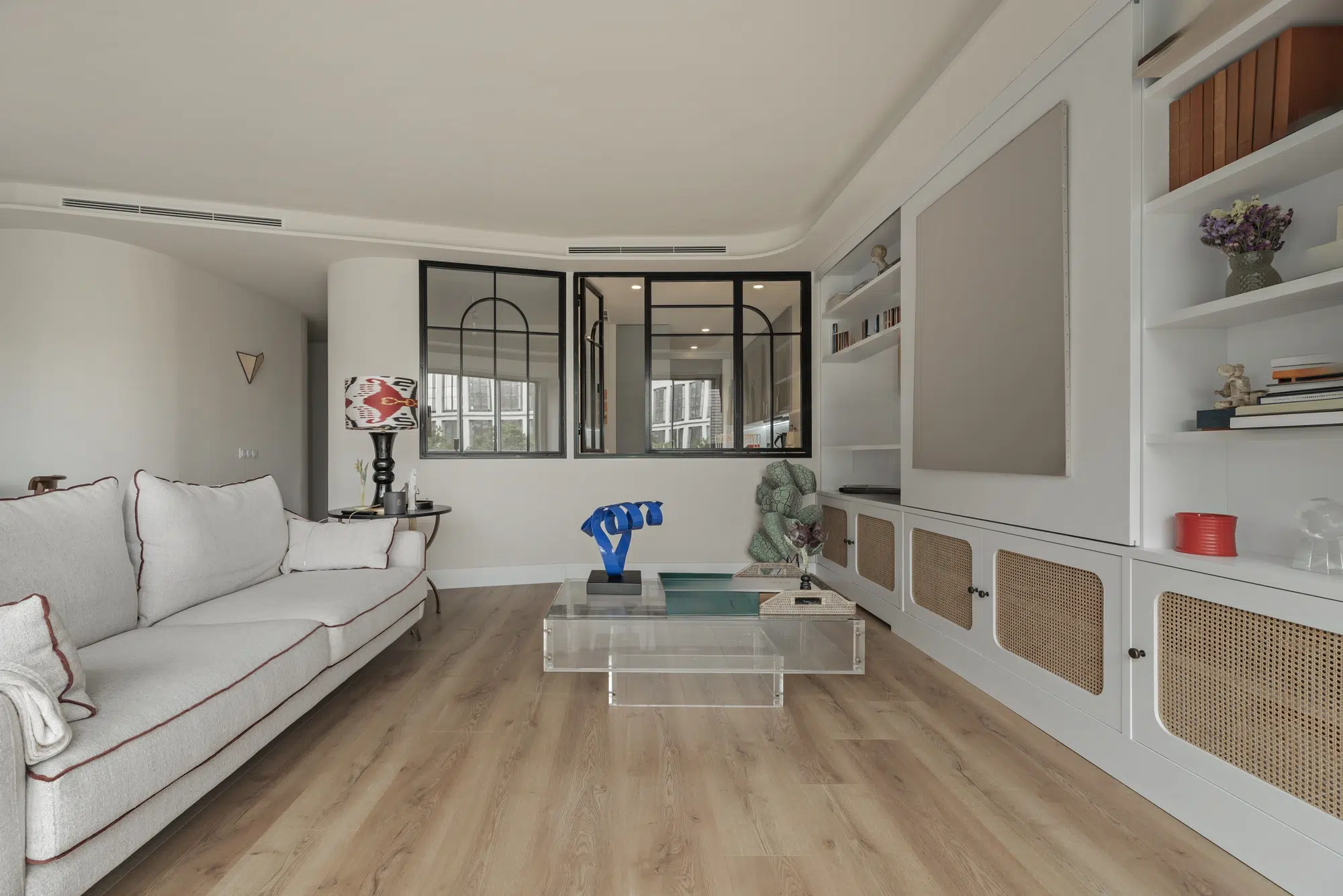 A living room with hardwood floors, a white couch, a glass table, and wicker cabinets on a white wall.