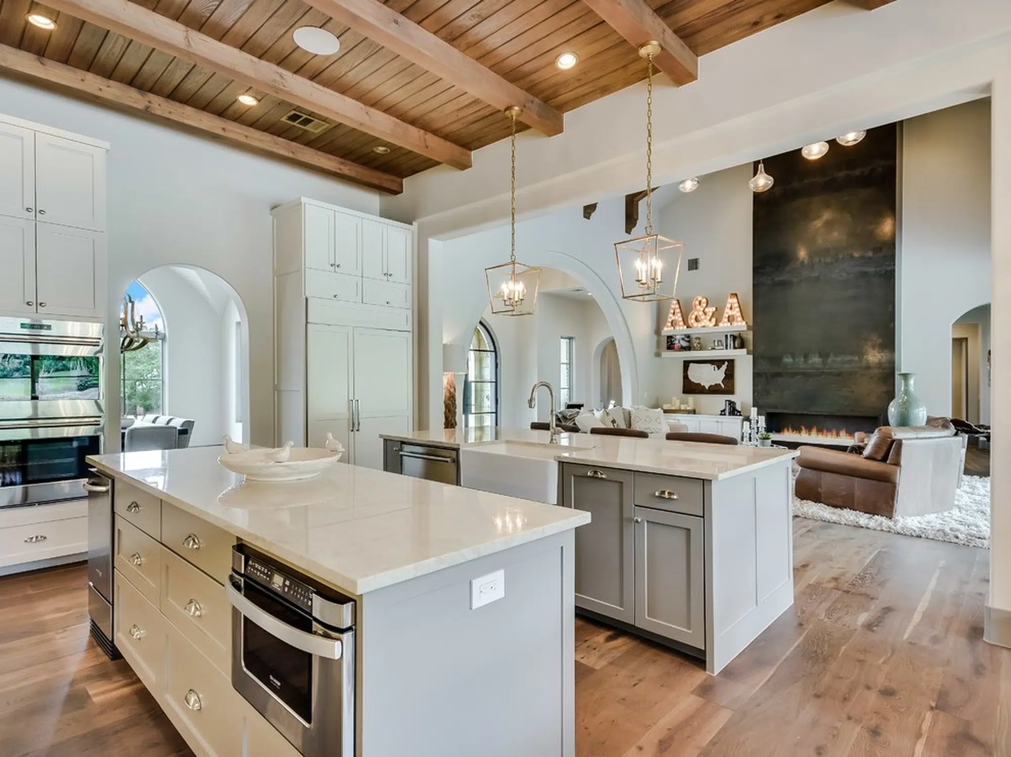 A white kitchen with hardwood flooring and a double island with marble countertops.