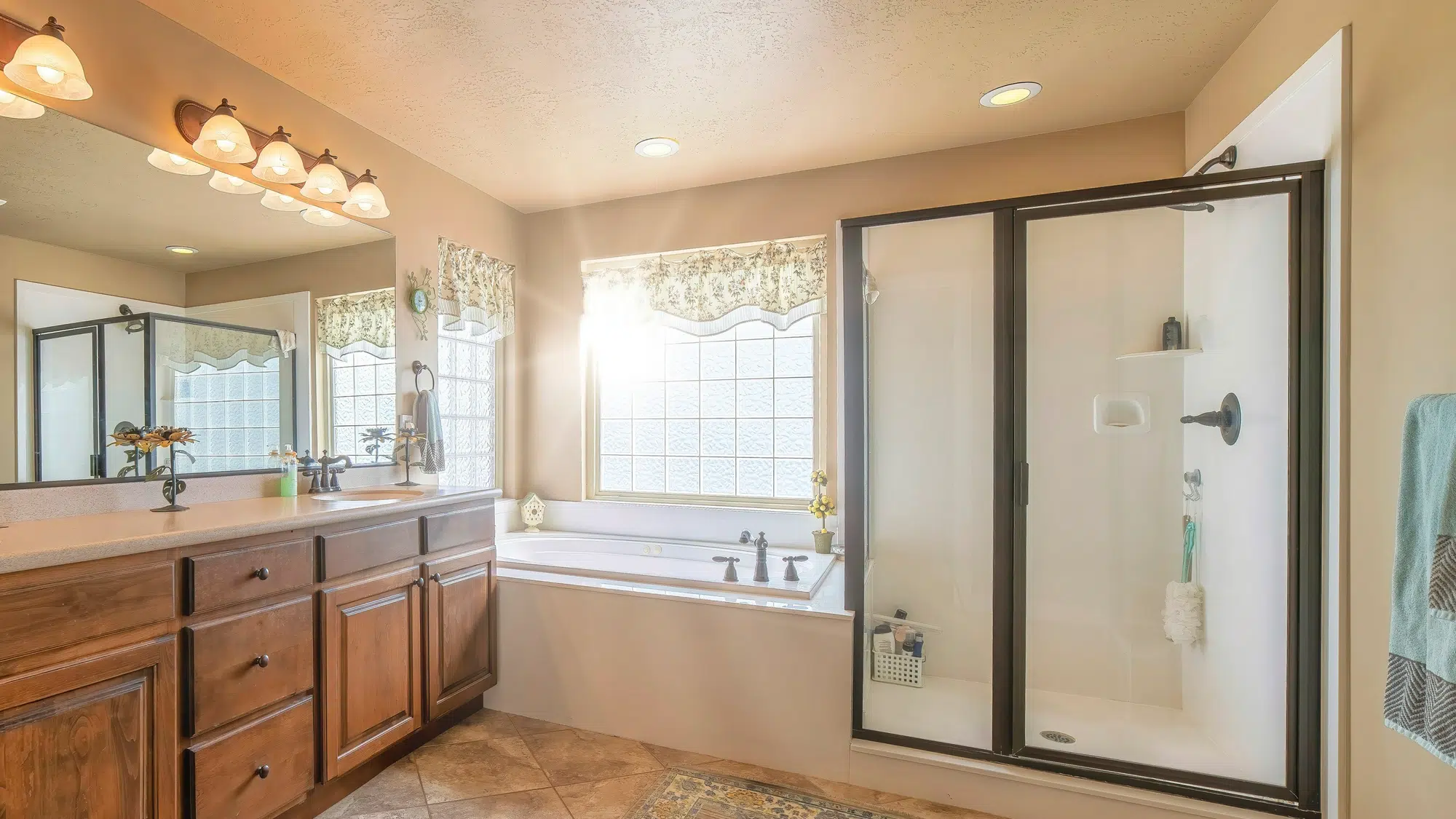 A bathroom with tile flooring, wood drawers, a marble vanity, a large mirror, a white bathtub, and a walk-in shower with a glass door.