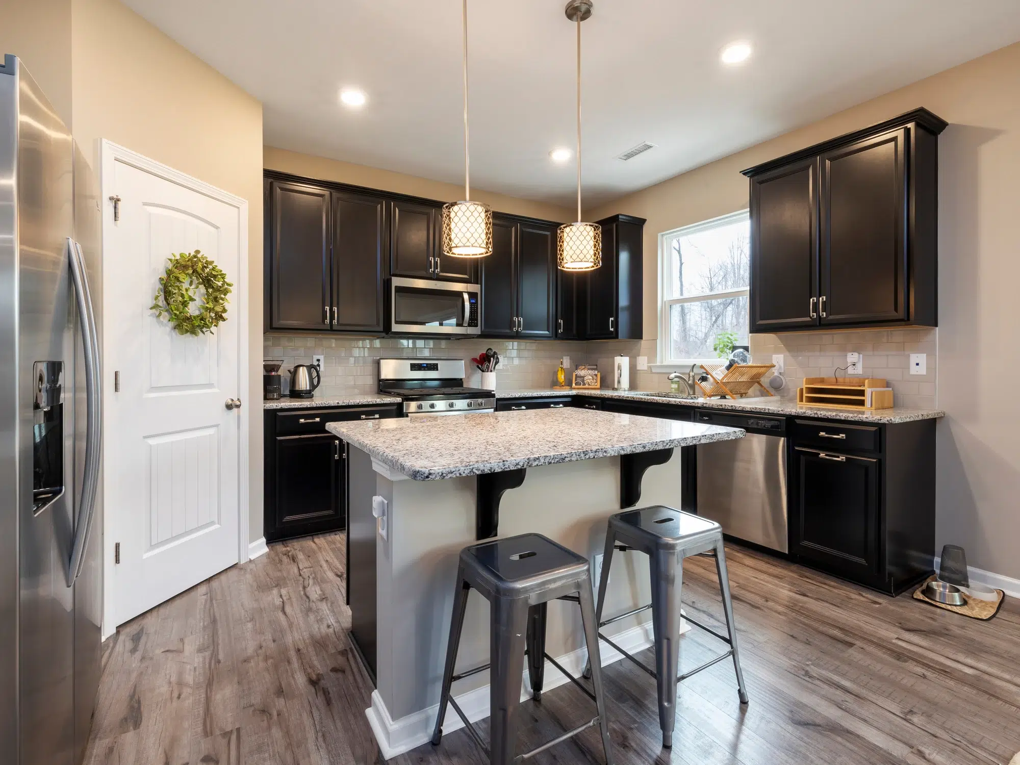 A kitchen with a marble island, gray stools, brown wooden cabinets, and steel appliances.