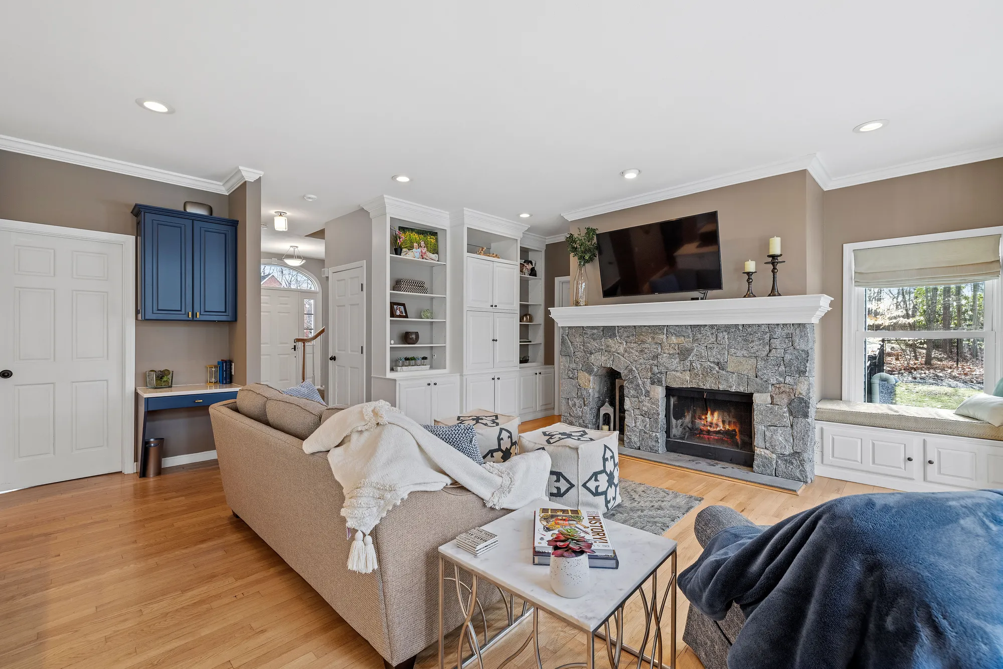 A living room with hardwood floors, a stone fireplace, a gray couch, and a television on the wall.