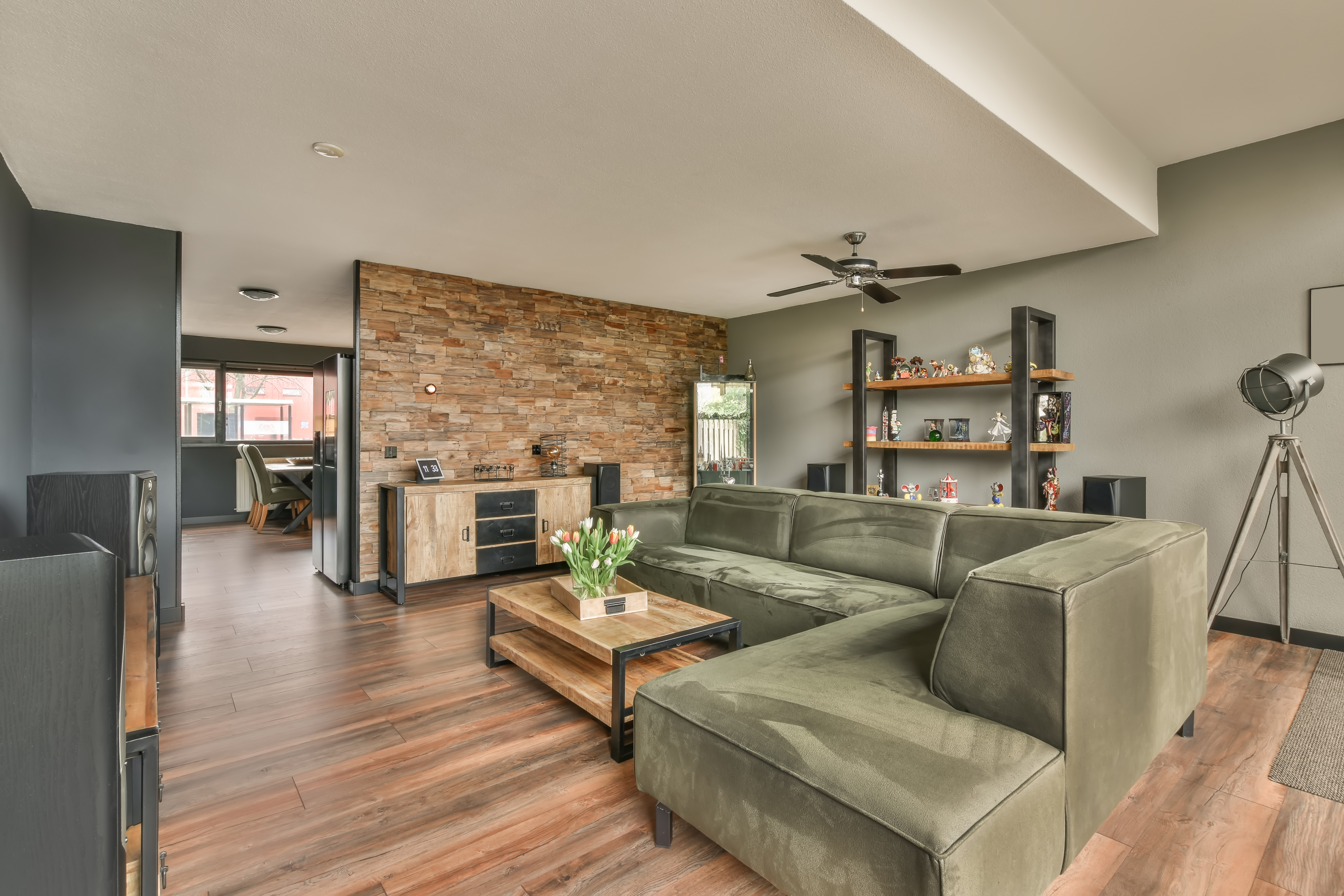 A living room with hardwood flooring, tan walls, a brown couch, and wood tables.