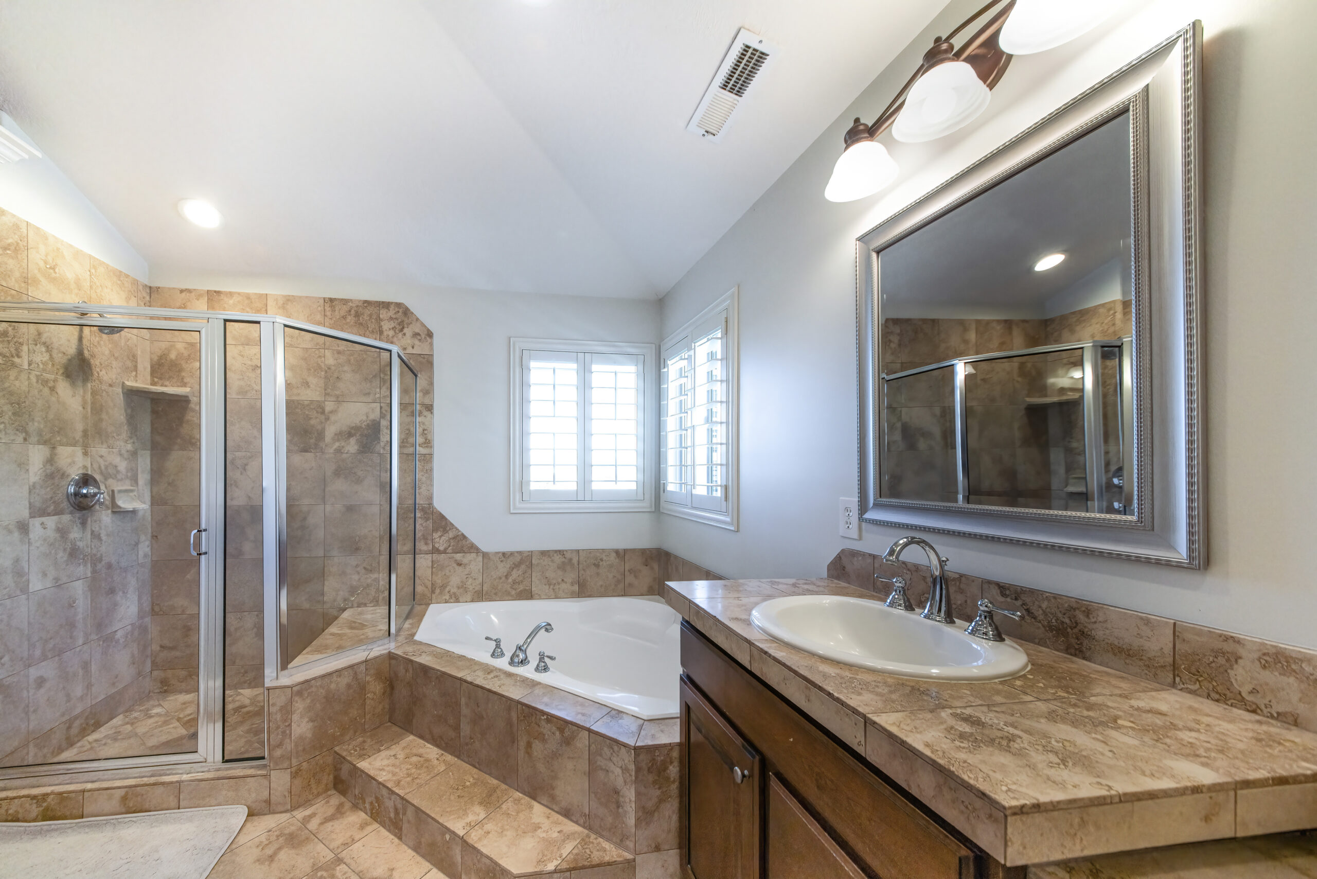 A bathroom with a marble vanity, a bathtub in the corner, and a walk-in shower with a glass door.