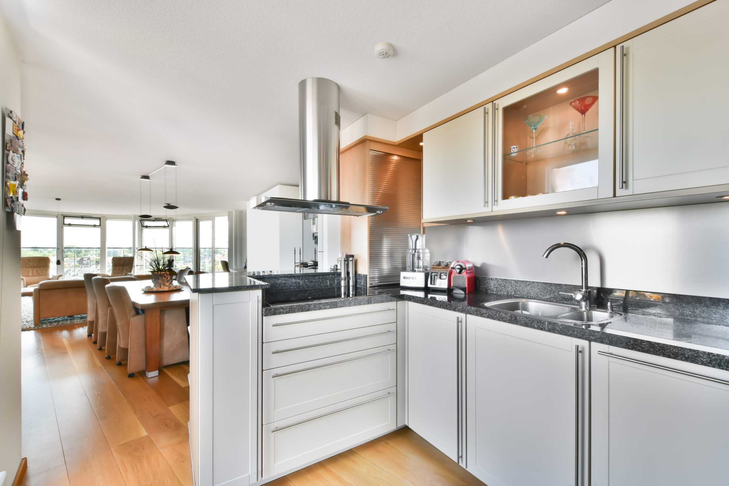 A kitchen with blue countertops, off-white drawers, and a dining room with windows in the background.