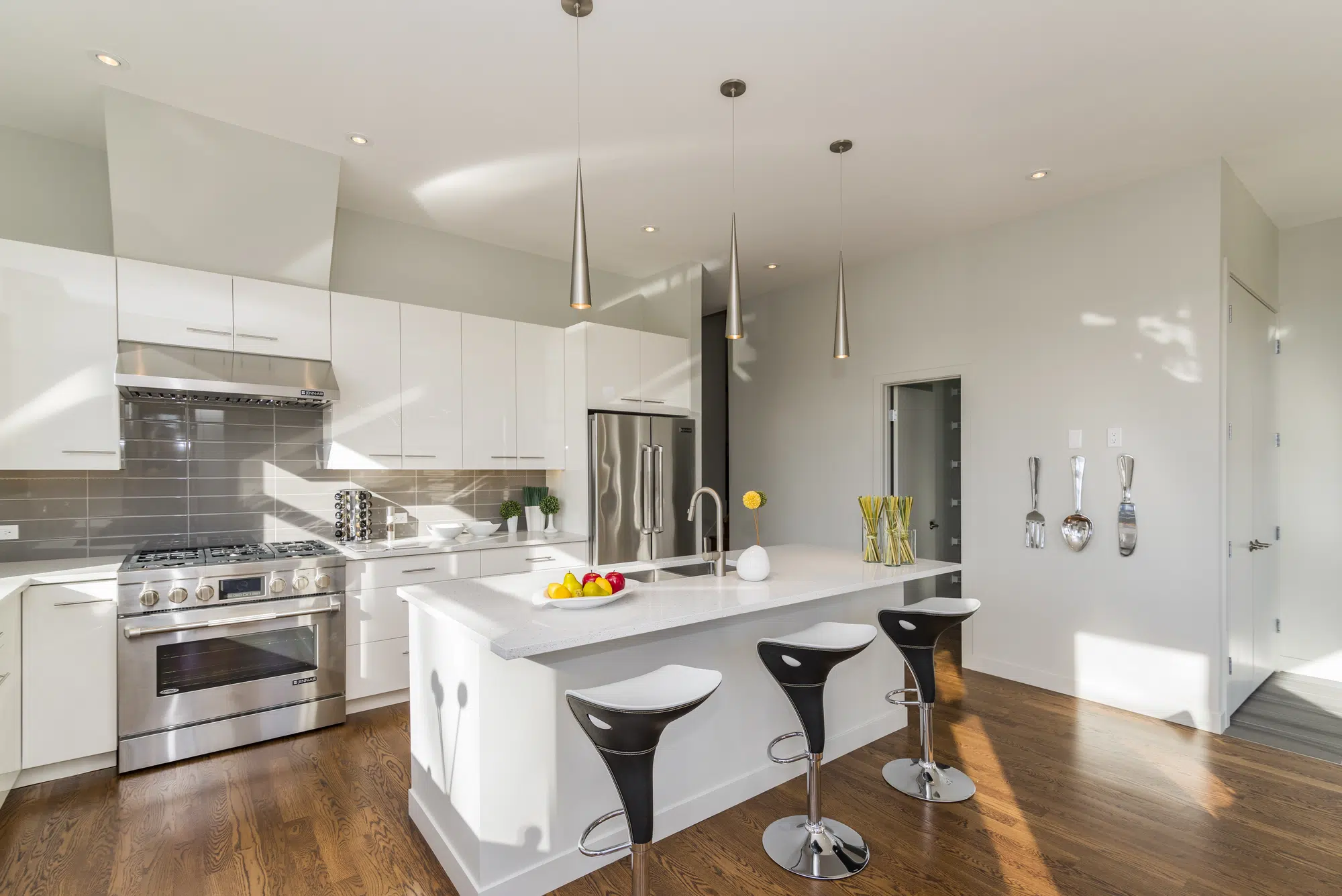 A bathroom with white walls, a white island, black seats, white cabinets, and steel appliances.