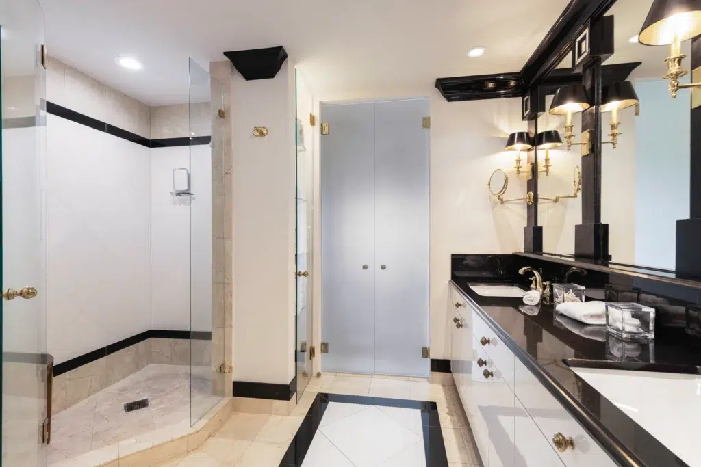 A bathroom with a black and white vanity, tile flooring, and a walk-in shower with a glass door.