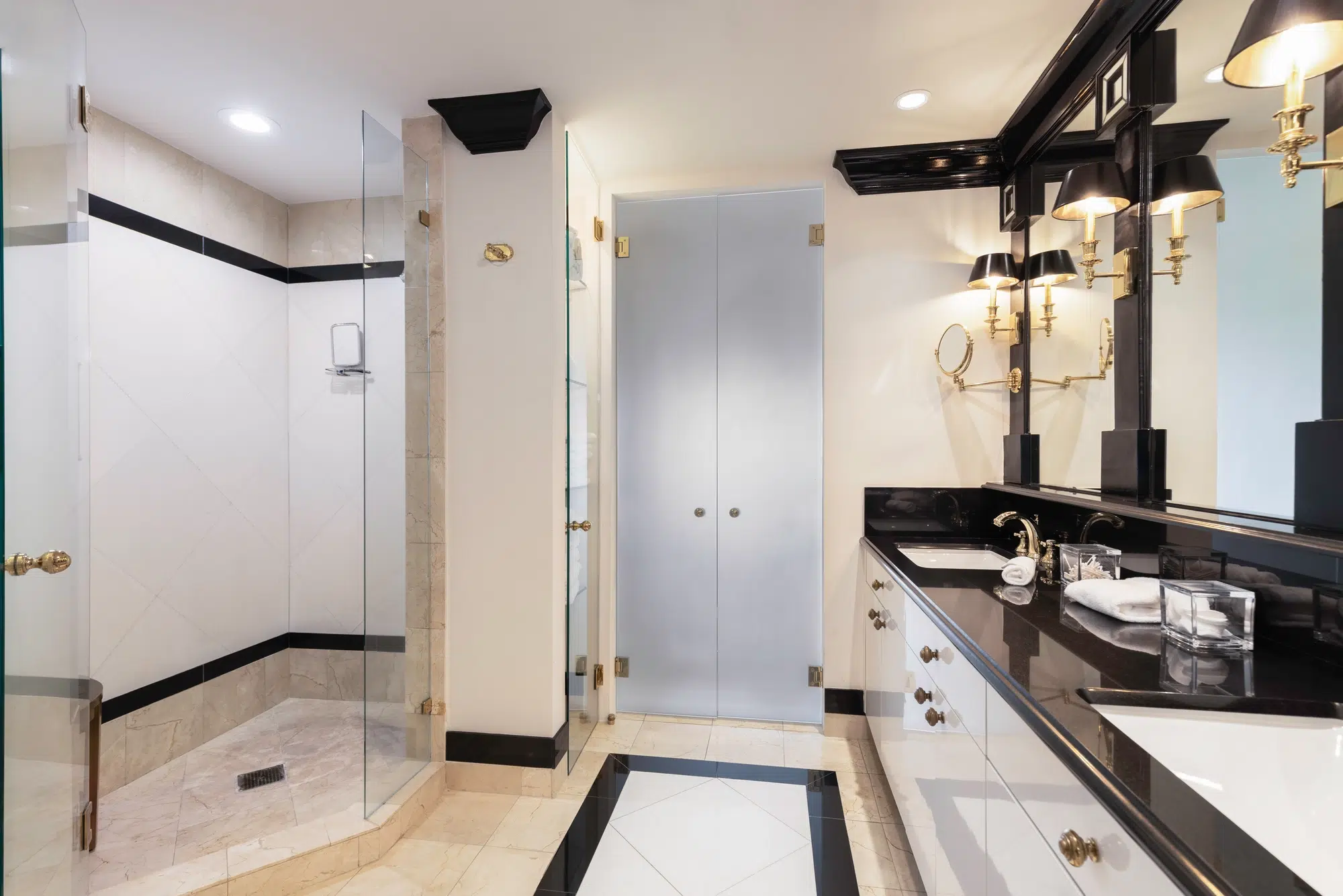 A bathroom with a black and white vanity, tile flooring, and a walk-in shower with a glass door.