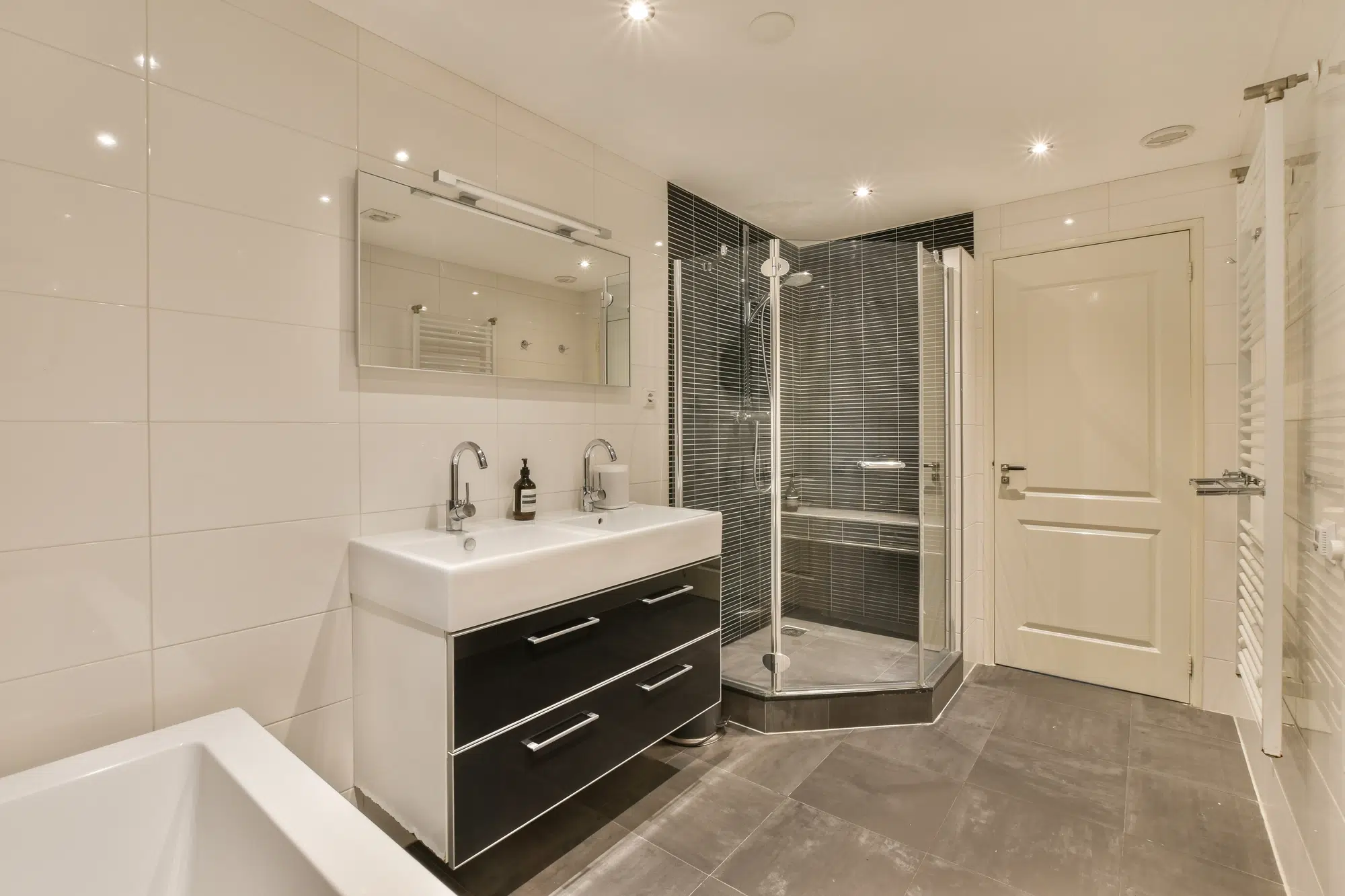 A bathroom with tile flooring, a white wall, a black vanity, and a walk-in shower with a glass door.