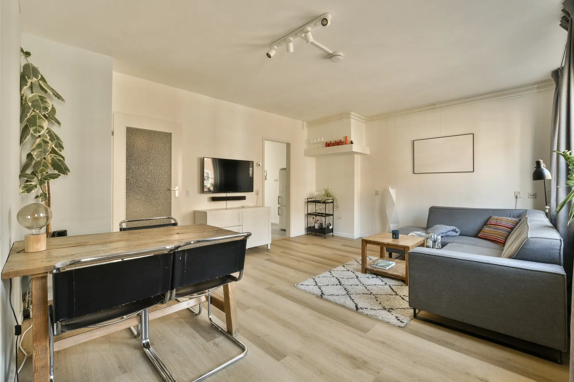 A living room with a blue couch, a wooden coffee table, a wooden dining table, and a television.