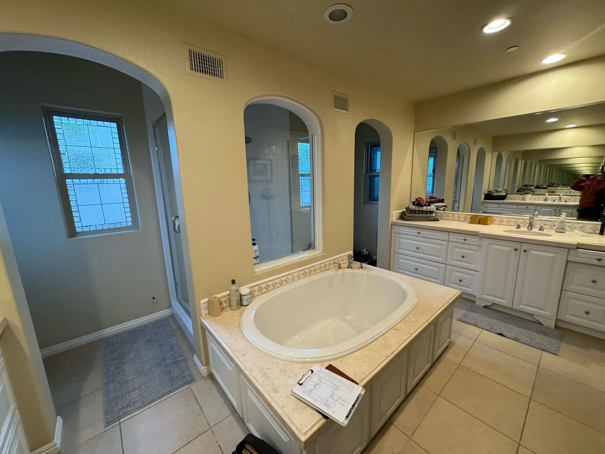 Modern bathroom with a freestanding black-and-white soaking tub, bold leaf-pattern wallpaper, gold fixtures, and a wooden vanity with a large mirror.