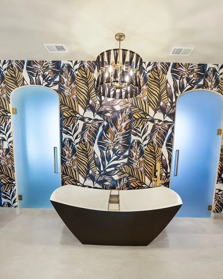 Freestanding black-and-white soaking tub centered in front of a bold leaf-pattern feature wall, with two frosted glass doorways.