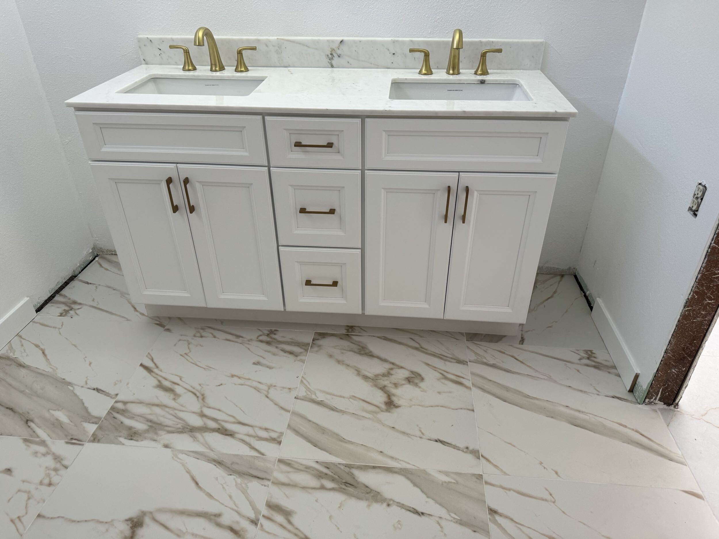 Elegant bathroom remodel in Signal Hill, CA, featuring a white double-sink vanity with gold faucets and handles, marble countertop, and large marble-look tile flooring