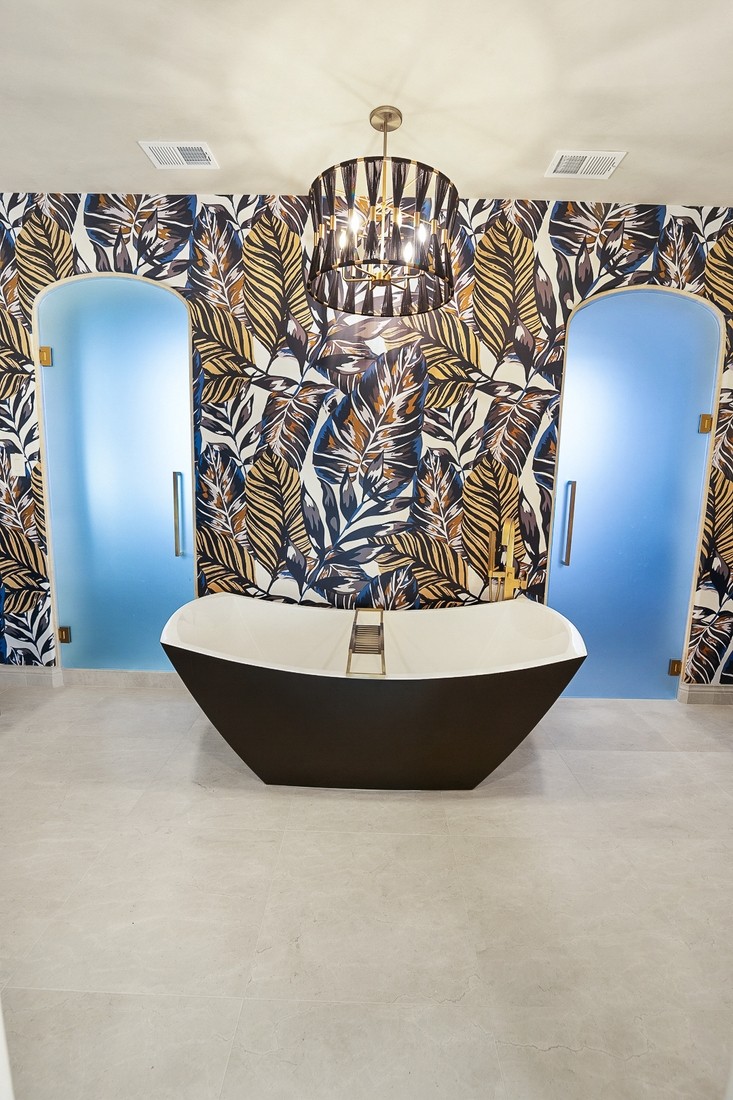 A bathroom remodel featuring a freestanding modern bathtub centered between two frosted glass doors,and bold tropical leaf wallpaper.