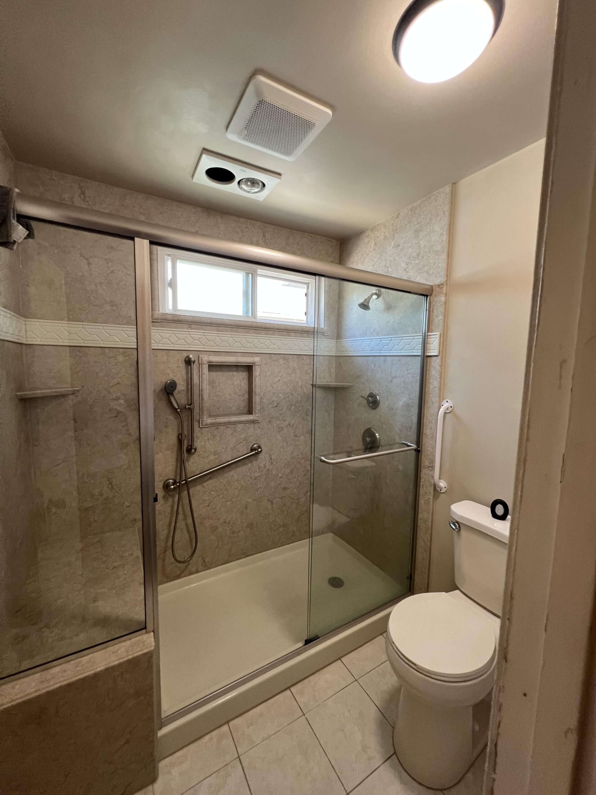 A modern walk-in shower featuring large gray tiles, gold trim accents, dual built-in niches, a frameless glass enclosure, and a marble-look tile floor.