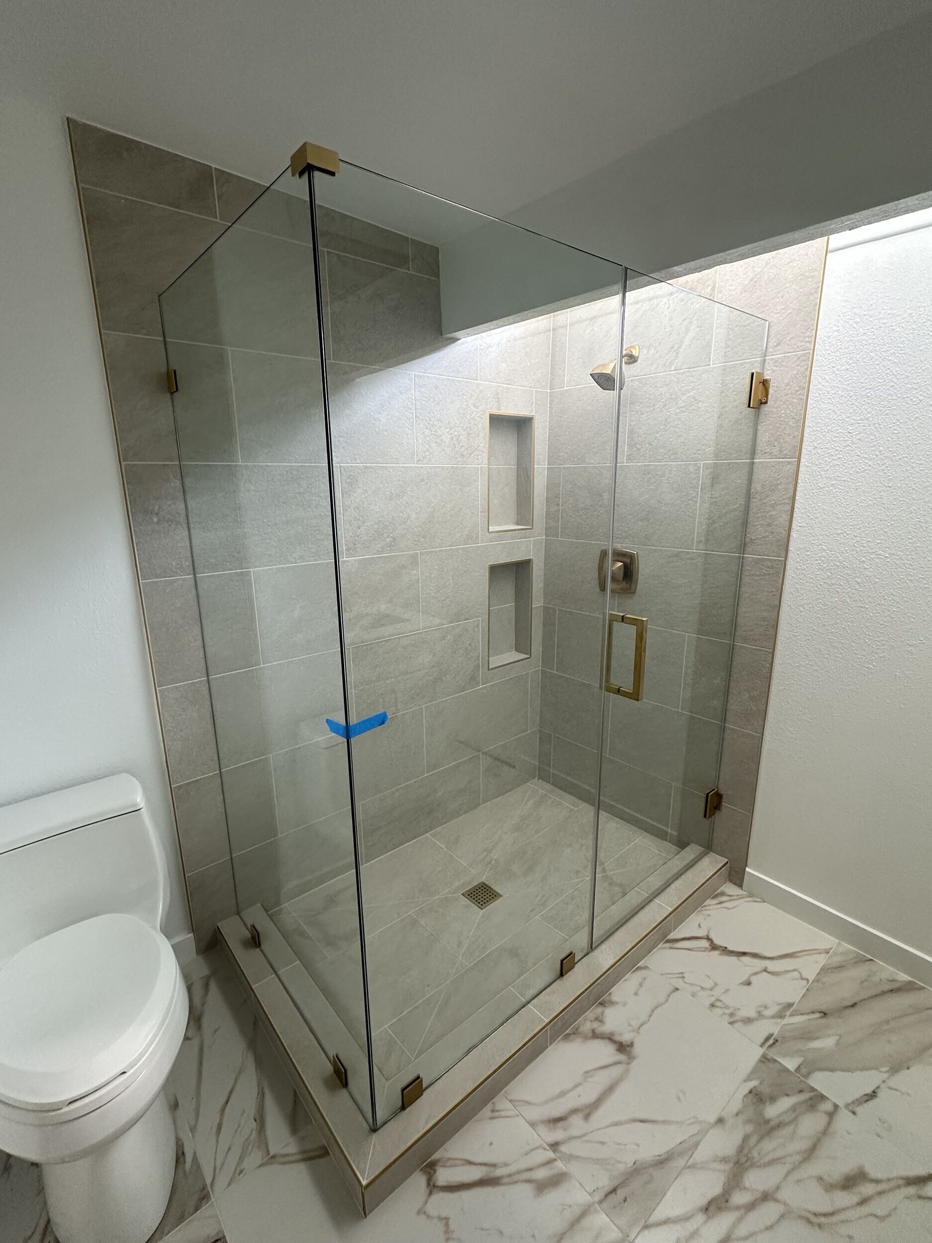 Modern bathroom featuring a frameless glass shower enclosure with gold hardware and beige wall tiles.