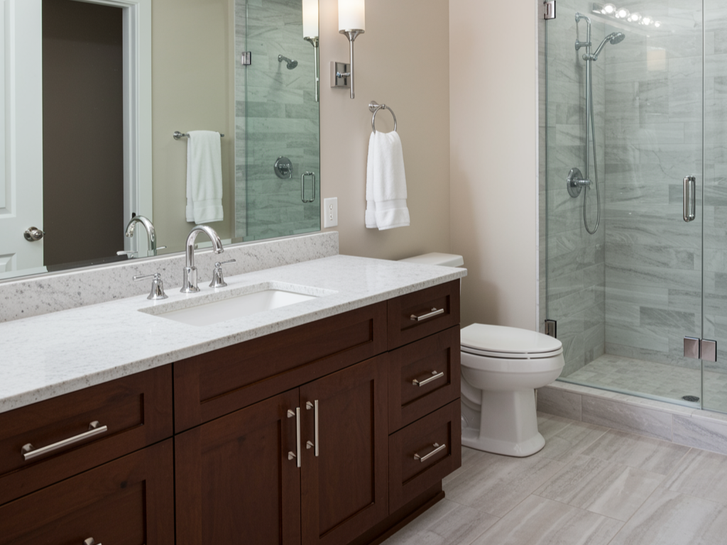 Modern bathroom with a dark wood vanity, white quartz countertop, chrome faucet, large mirror, toilet, and a glass-enclosed shower.