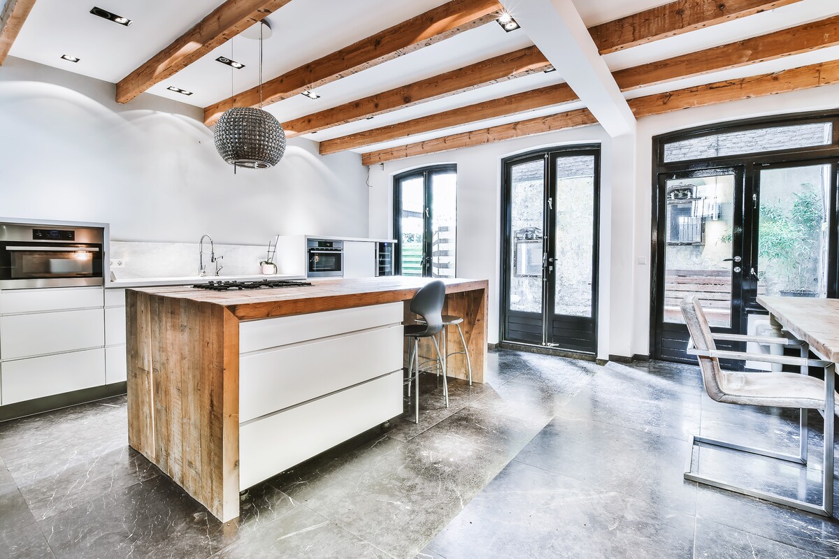 Modern home remodel featuring exposed wood beam ceilings, custom kitchen island, sleek white cabinetry, dark stone flooring and pendant lighting.