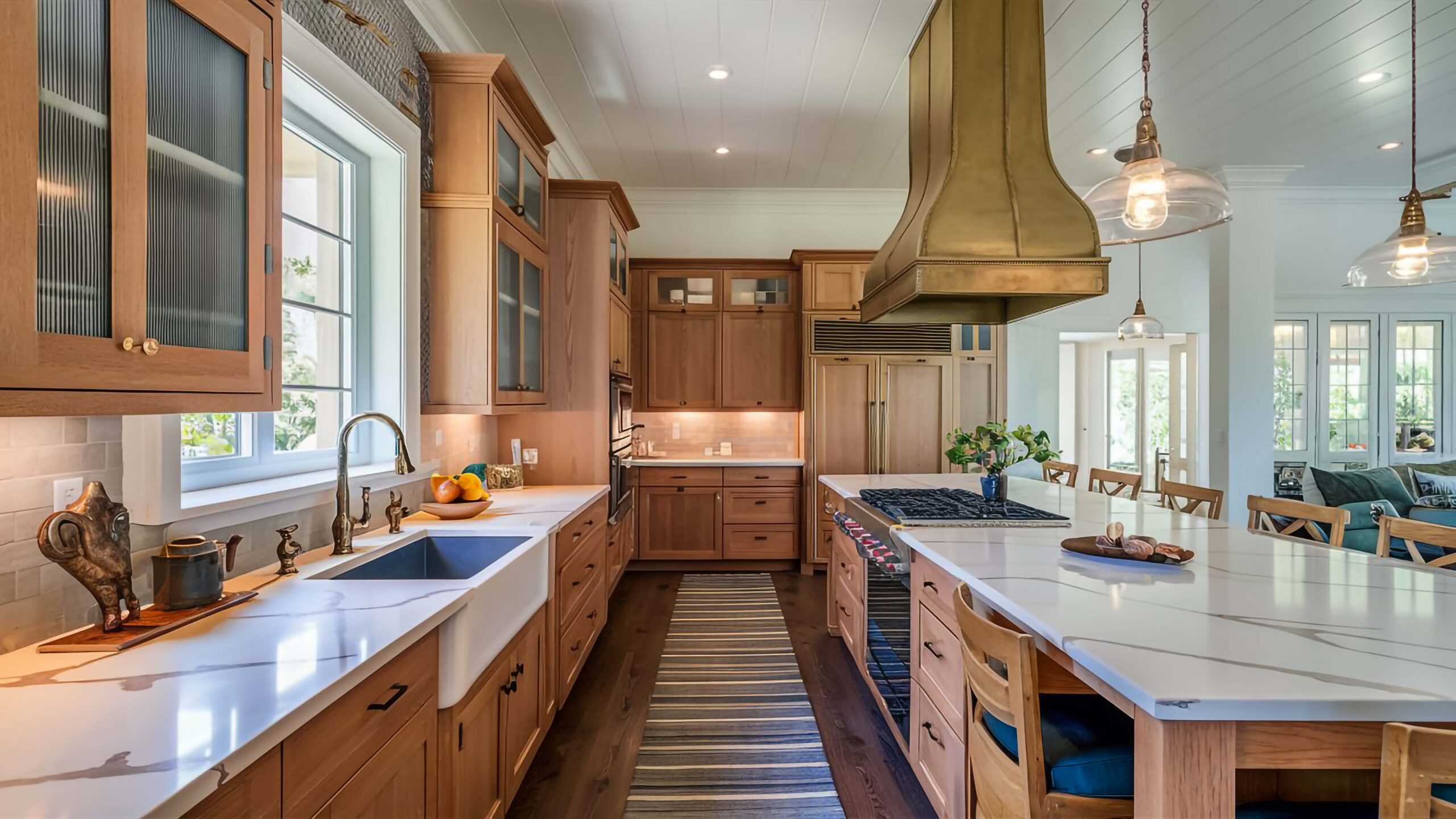 Open remodeled living space with wood-look flooring, gray walls, white trim, recessed lighting, large windows, and a kitchen visible in the background.
