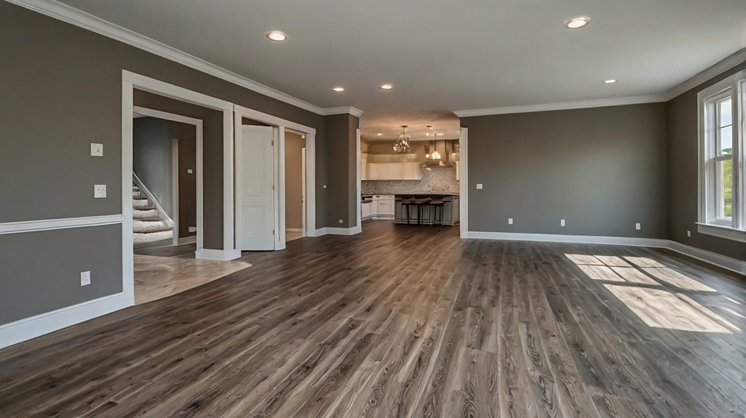 Modern white kitchen with island seating, stainless steel appliances, pendant lights, gray backsplash, wood floors, and bright natural light.