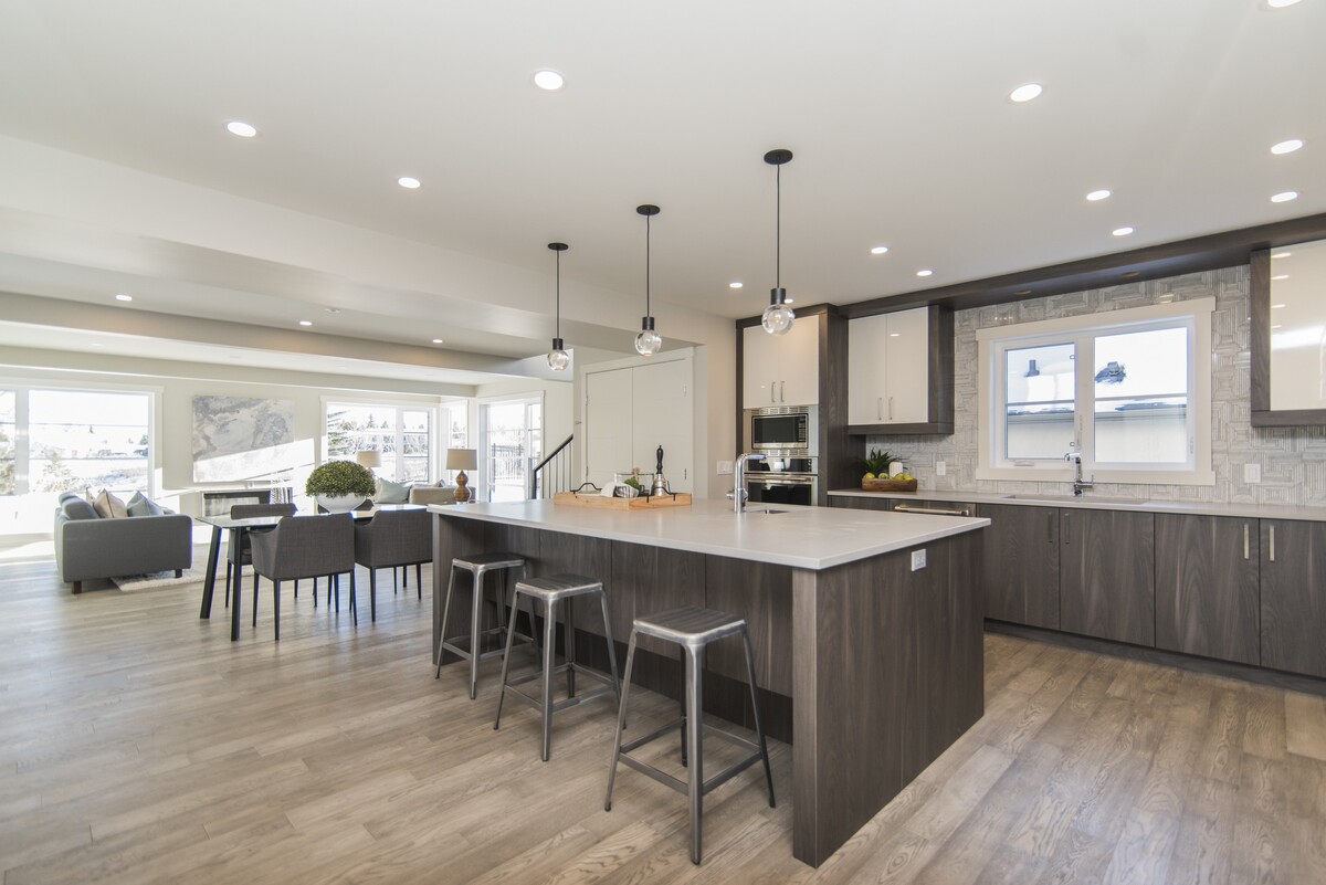 Open-concept modern kitchen remodel with large island, dark wood cabinetry, pendant lighting, built-in appliances, and adjoining living space.
