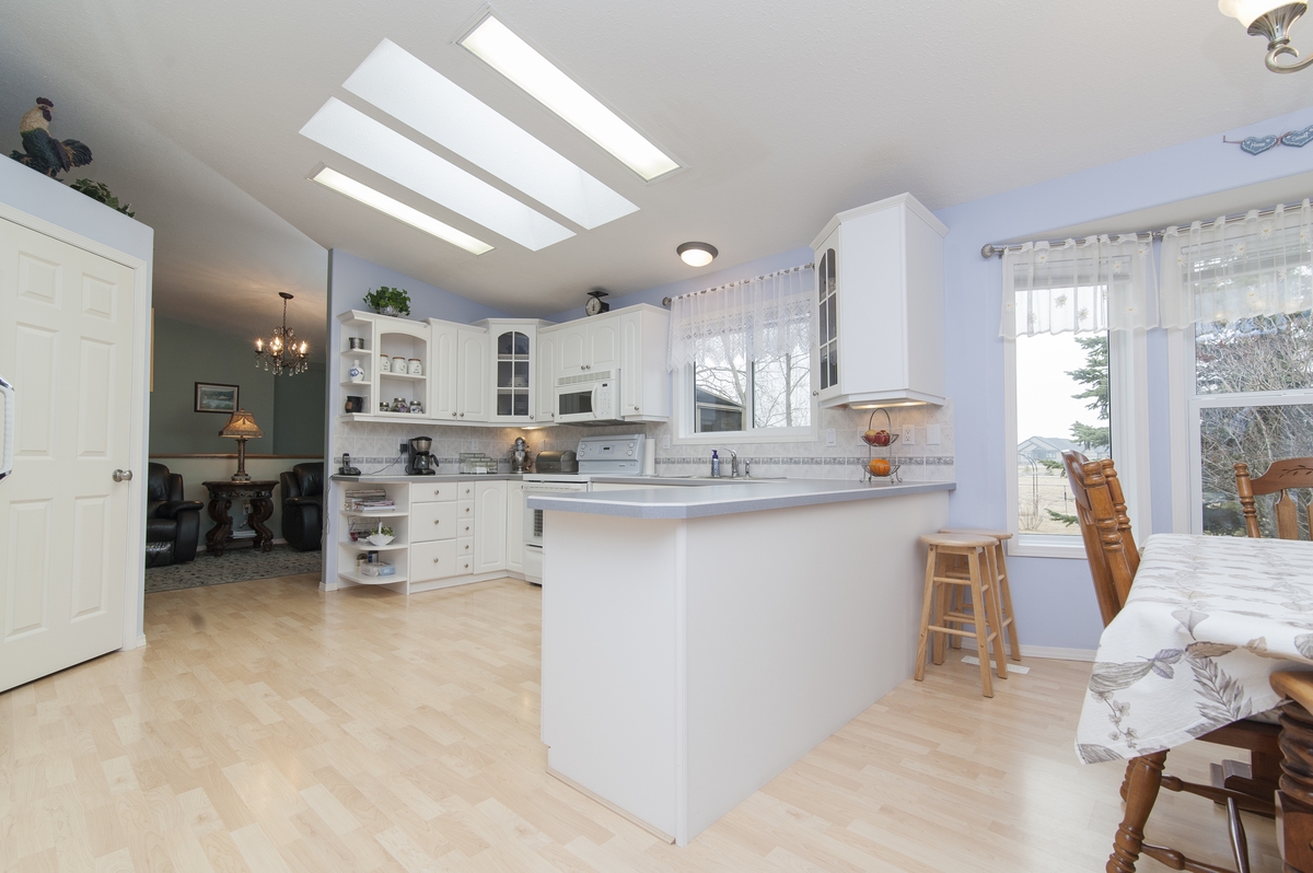 A bright, open-concept kitchen features white cabinetry, a large peninsula with barstools, and light wood flooring updated during a professional kitchen remodeling project.