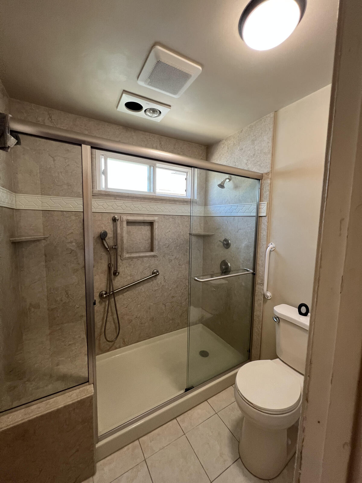 A bright, modern bathroom featuring a large glass-enclosed shower with teal subway tile, white scalloped accent tile, and pebble flooring.