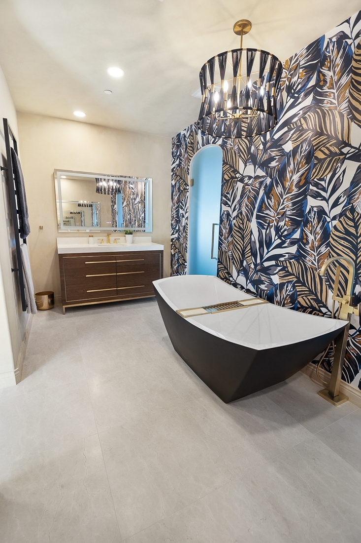 A luxurious freestanding black and white bathtub, vibrant tropical leaf finish, and elegant gold fixtures create a stunning oasis in this professional bathroom remodeling project.