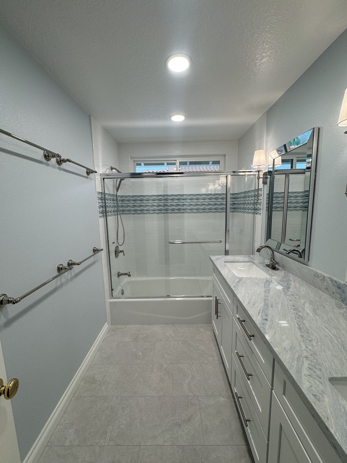 A modern bathroom features light blue walls, a long marble-topped vanity, and a clean glass-enclosed shower and tub area completed during a professional bathroom remodeling project.